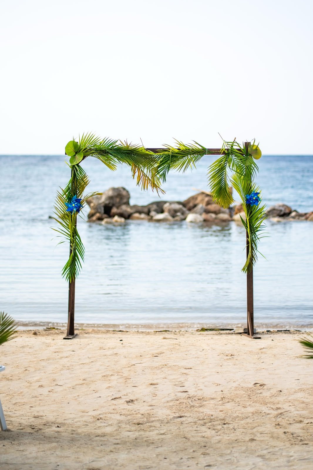 A decorated wedding arch on a sandy beach with the ocean and rocks in the background.