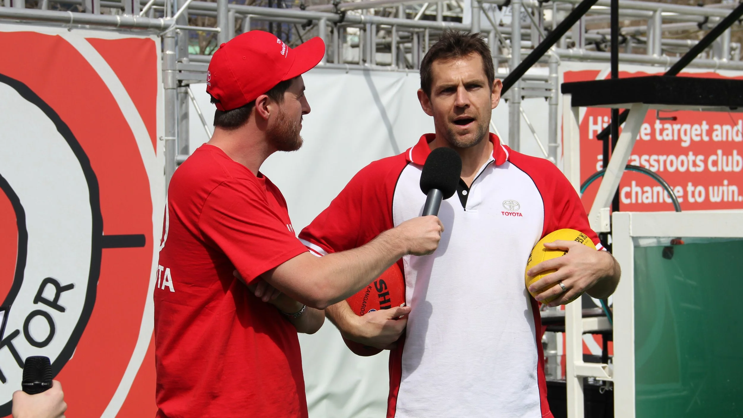 Man interviewing an Australian rules football player holding a yellow football at a sporting event