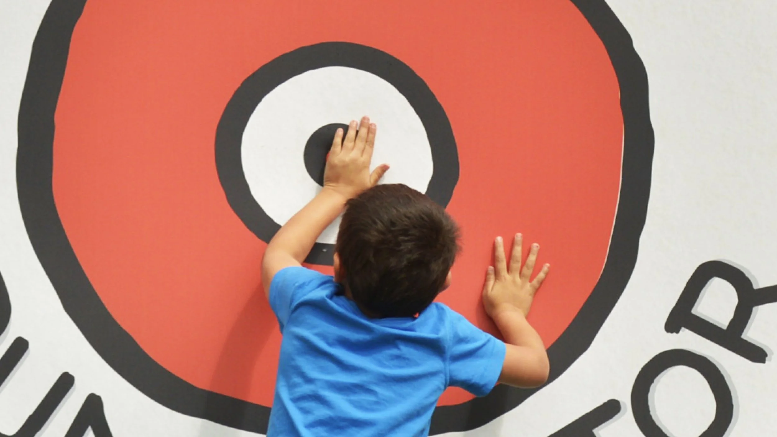 Child in a blue shirt reaching toward the center of a large red-and-black target.