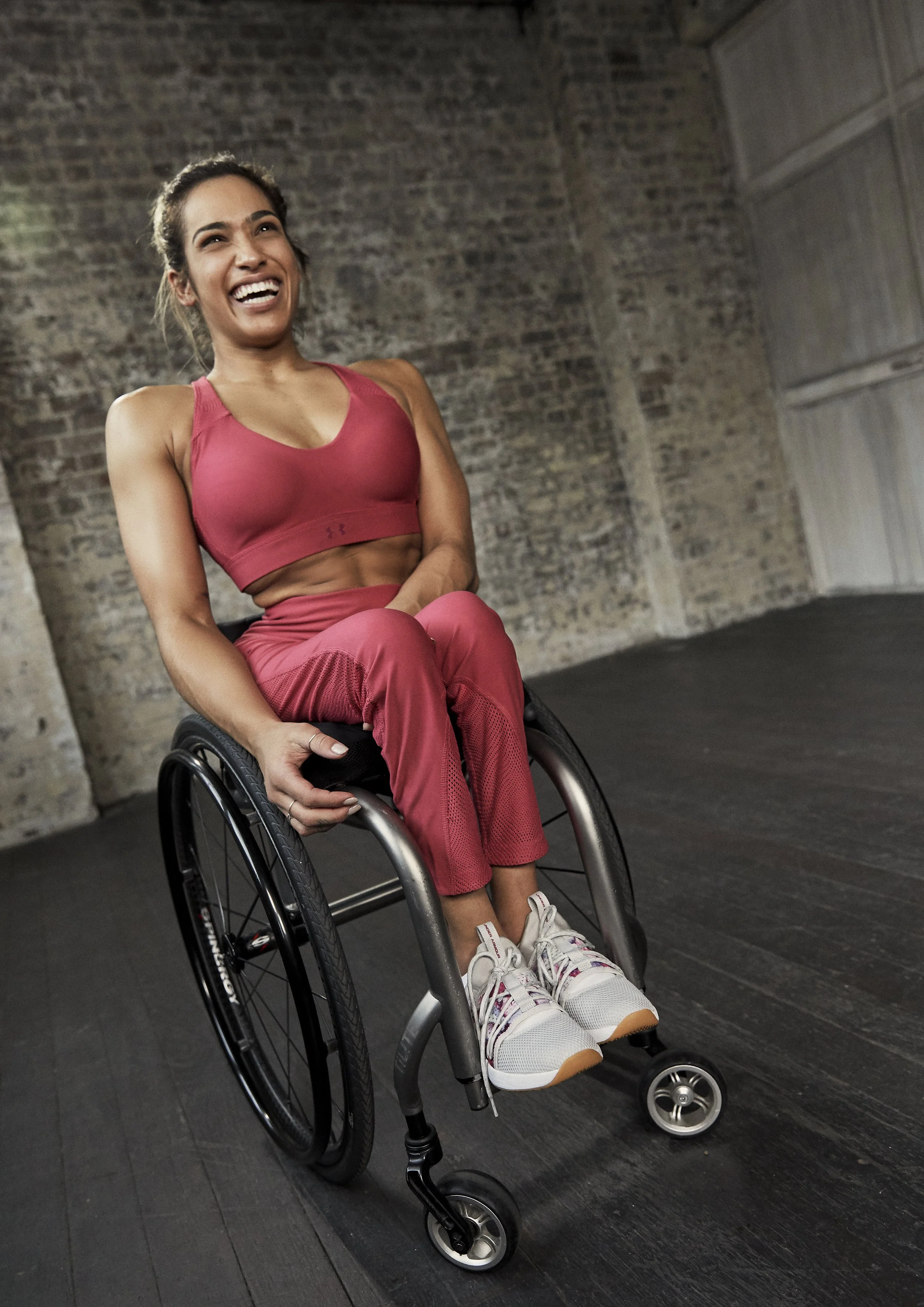 Smiling woman in pink athletic clothing seated in a wheelchair indoors