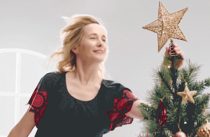 Smiling woman placing a star topper on a decorated Christmas tree
