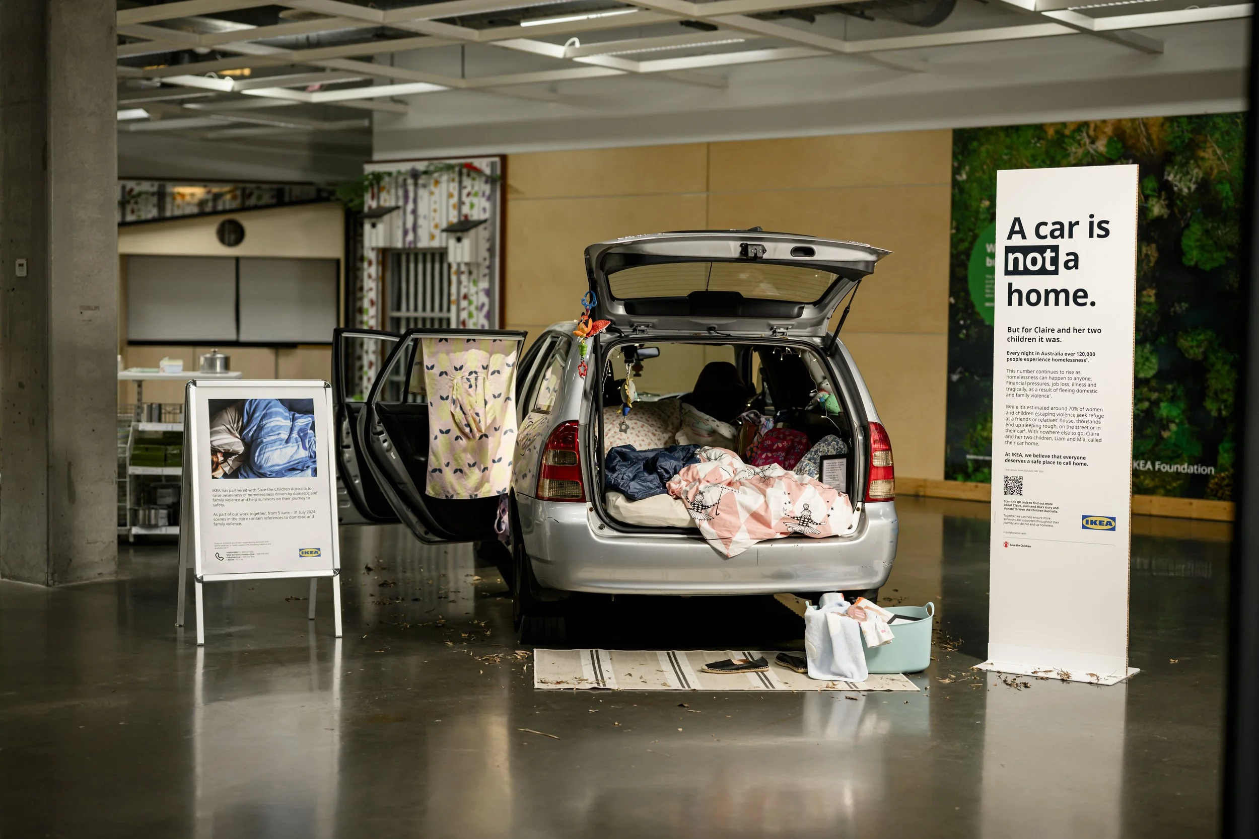 IKEA homelessness awareness display featuring a car filled with bedding and belongings, with a sign reading “A car is not a home.”