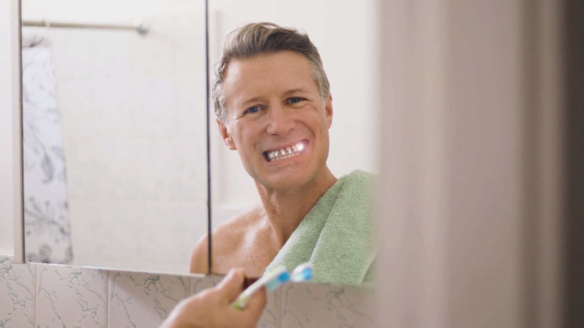 Smiling man with dental braces brushing his teeth in a bathroom mirror