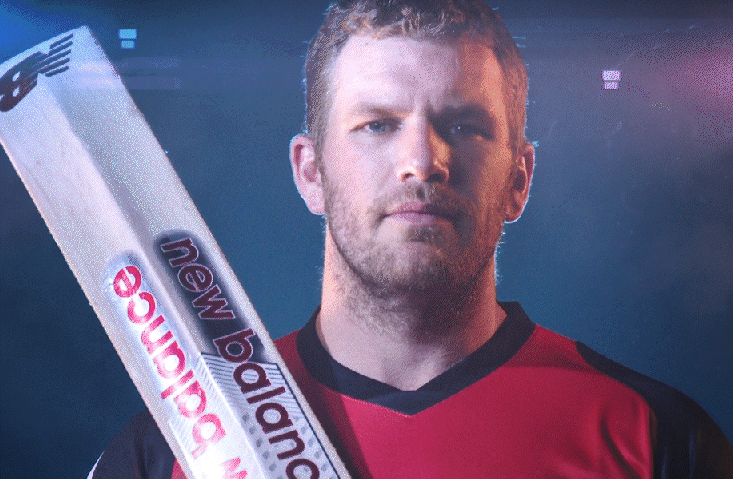 Cricketer holding a cricket bat labeled New Balance against a dark background