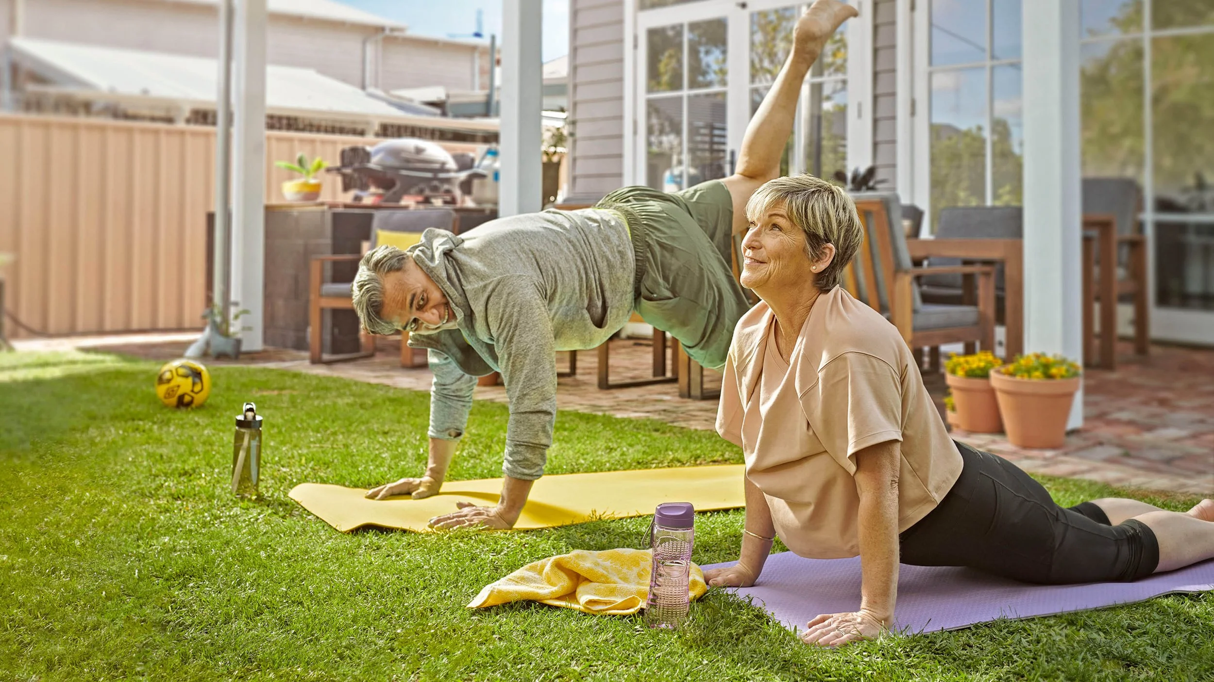 Older couple doing yoga exercises on mats in a sunny backyard patio