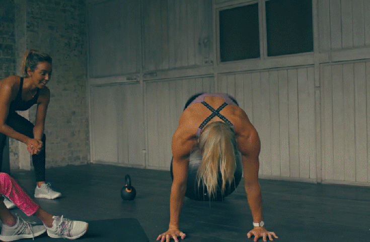 Women exercising in a fitness studio, with one performing a bear crawl beside a kettlebell.