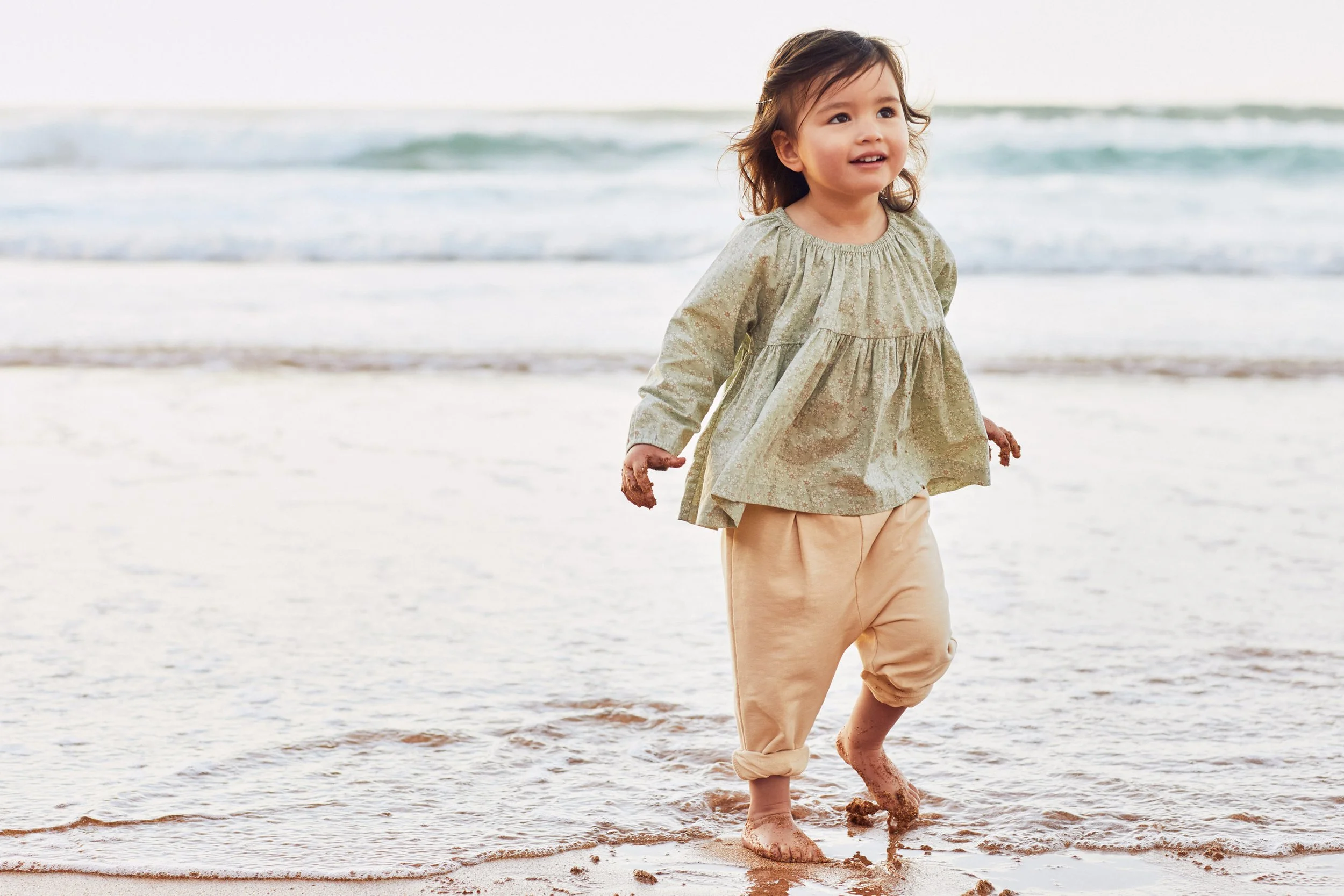 Young child walking barefoot in shallow ocean water at the beach