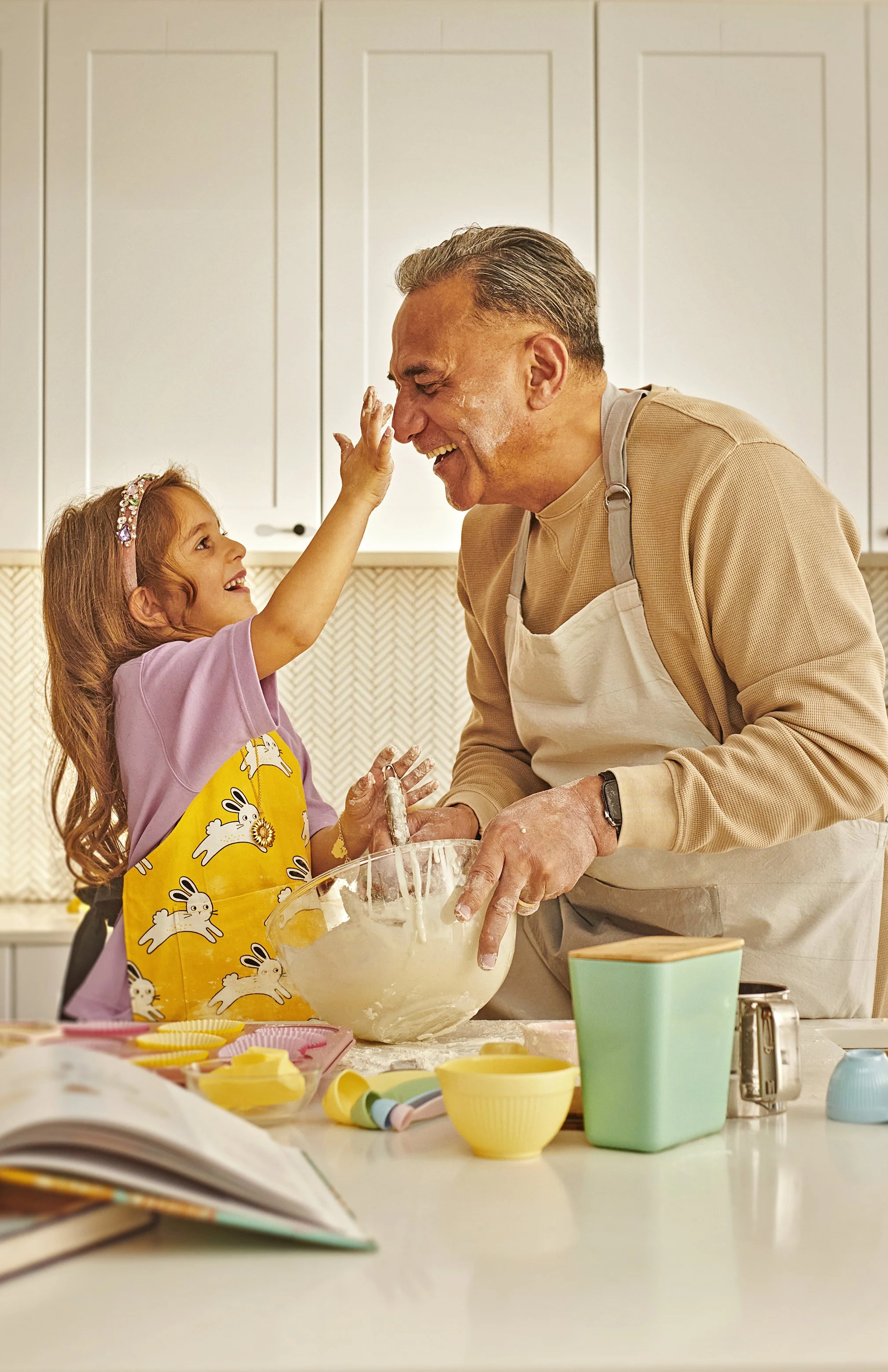 Grandfather and granddaughter baking together in a kitchen, mixing dough in a glass bowl.