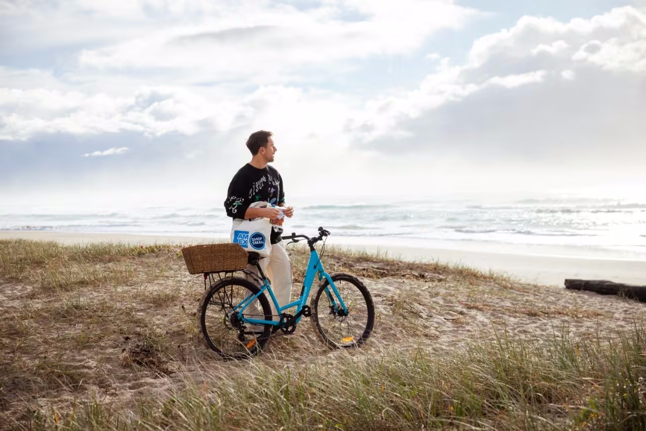 Man standing with a blue bicycle on a sandy beach beside the ocean