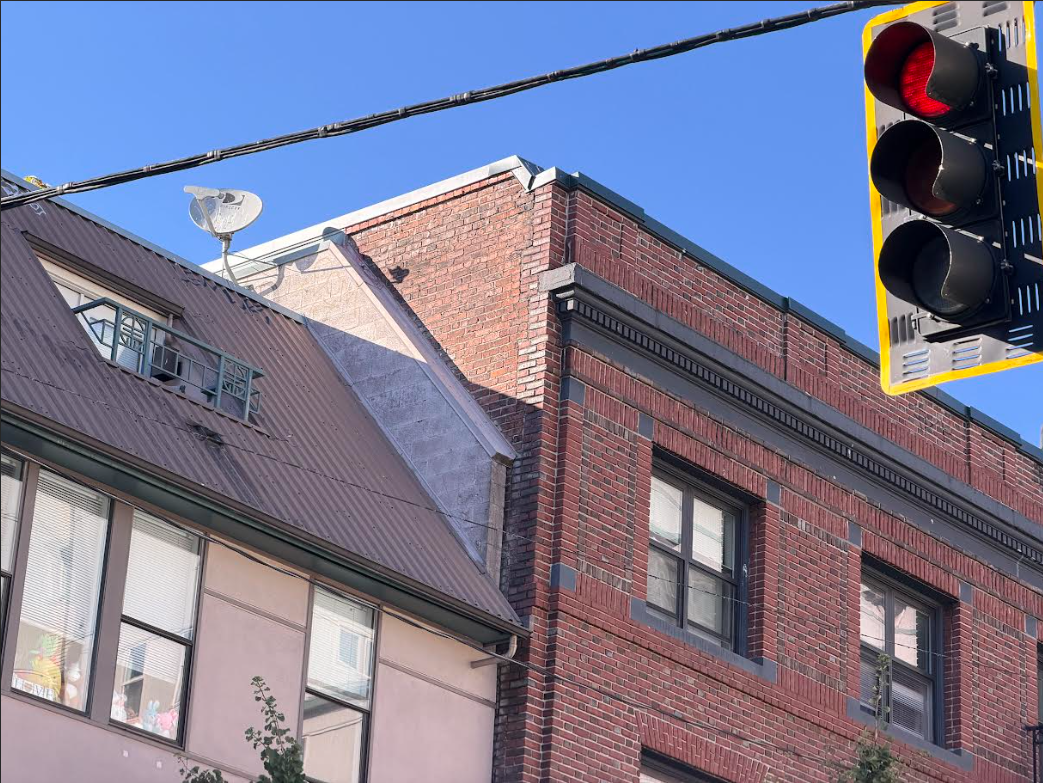Empty traffic light with red signal over a city street, brick and concrete buildings, and a clear blue sky.