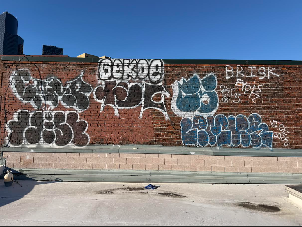 Graffiti art on a red brick wall with various tags, bubble letters, and designs in black, white, and blue, over a bright blue sky.