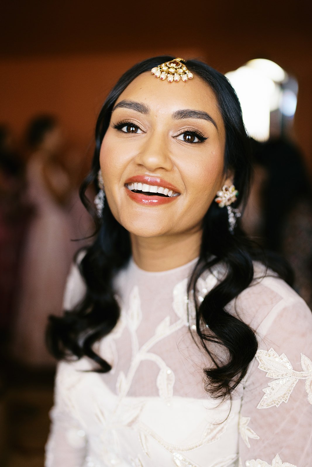 A woman with dark hair and light makeup smiling at a formal event, wearing traditional jewelry and an elegant outfit.