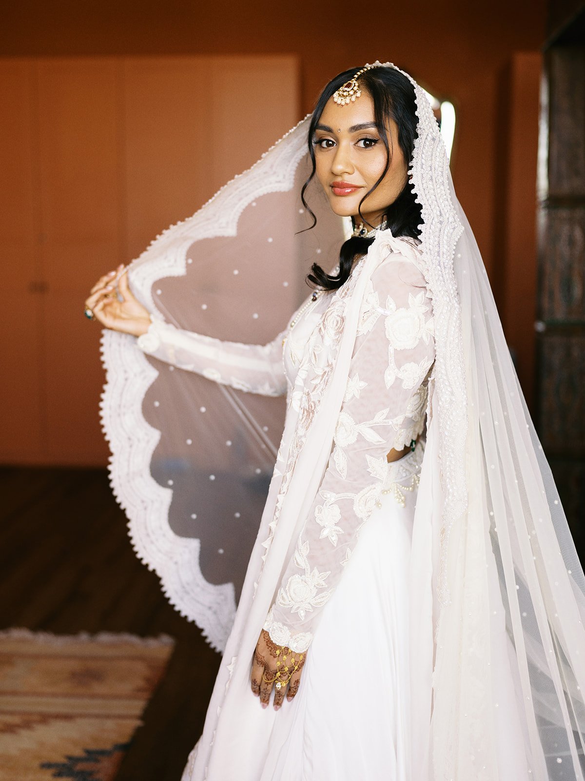 A woman wearing a white wedding dress with embroidery holding a lace umbrella.