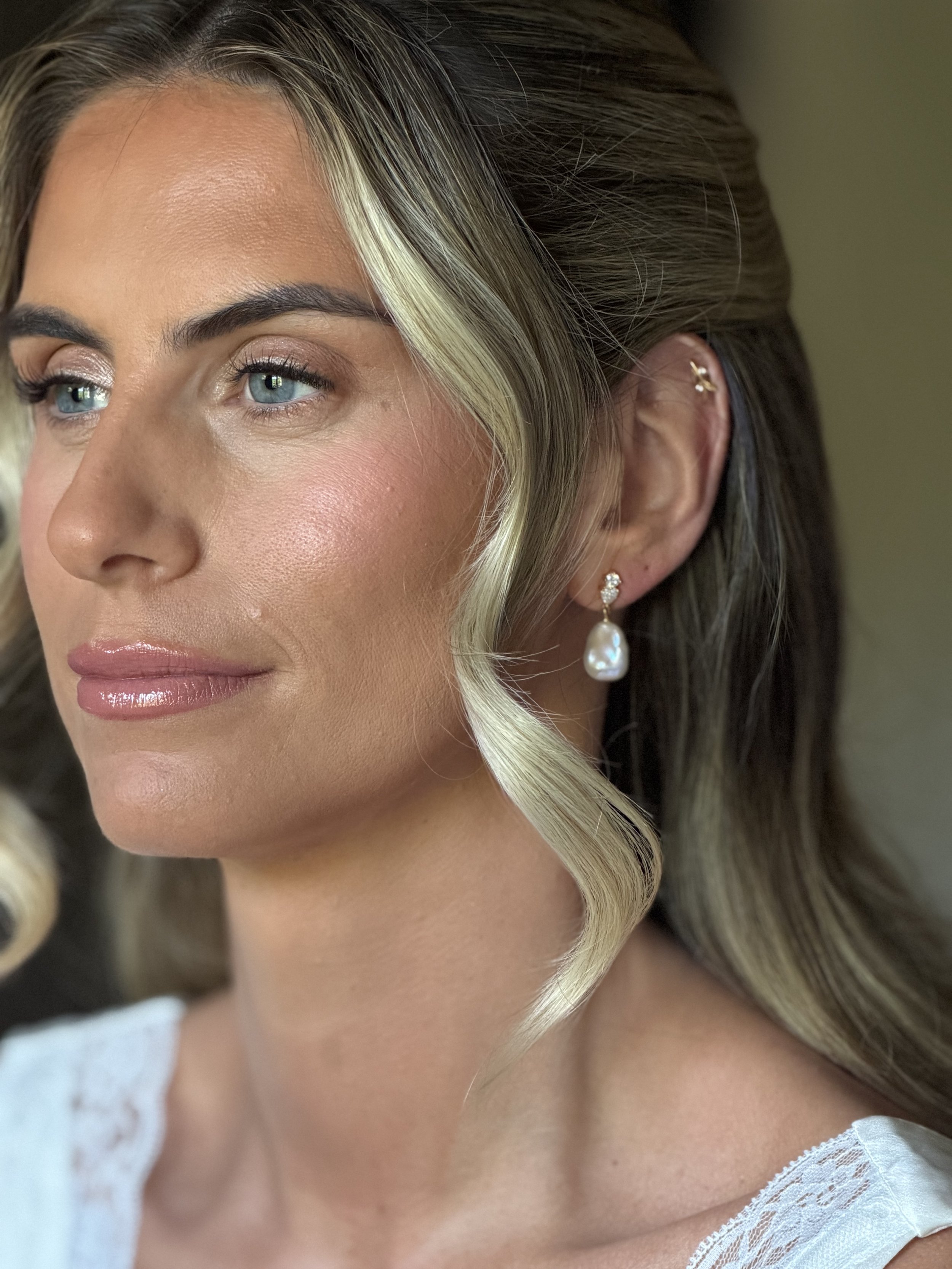 Close-up of a woman's face showing part of her left eye, cheek, and ear with jewelry, and styled hair with blonde highlights.