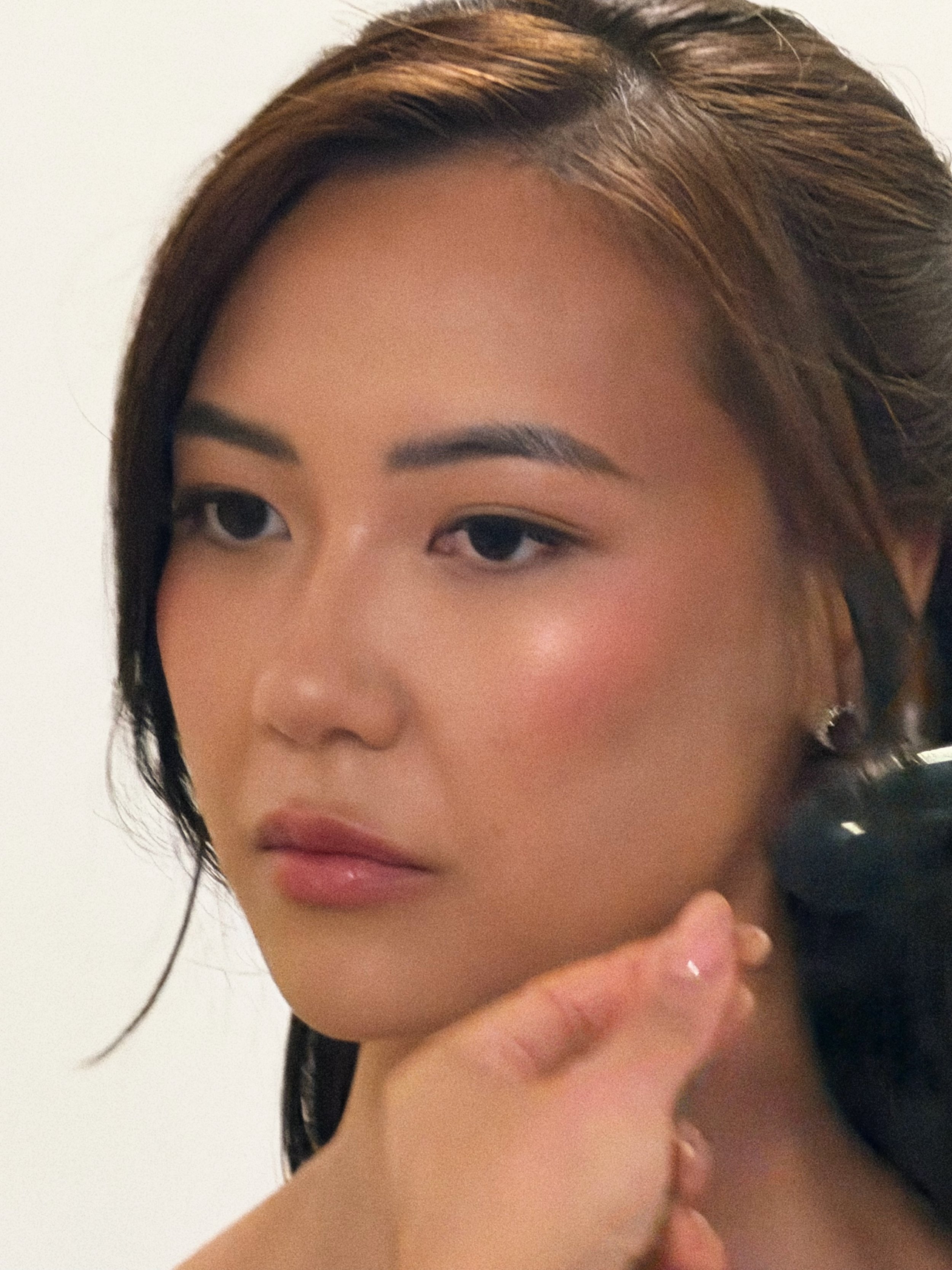 Close-up of a woman's face with makeup, including eyeliner, eyeshadow, and lipstick, with her hand gently touching her chin and hair styled with brown highlights.