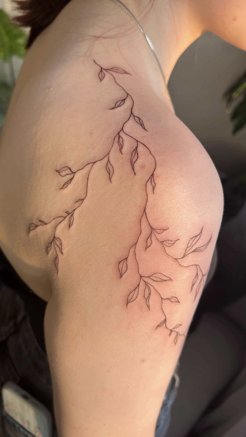 Nahaufnahme eines filigranen botanischen Tattoos mit Blüten und Blättern am Oberarm.