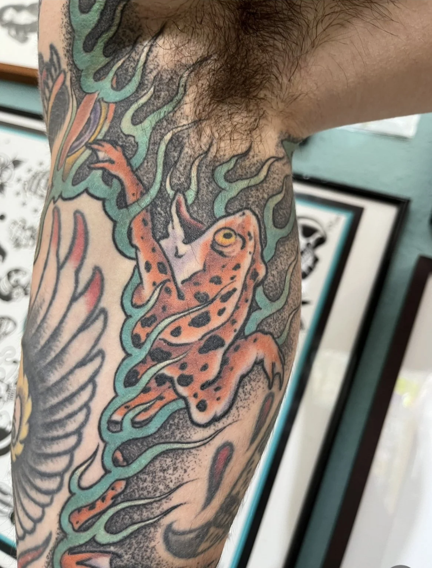 Nahaufnahme eines bunten Unterarm-Tattoos mit einem orangefarbenen Leoparden zwischen grünen Ranken und floralen Motiven