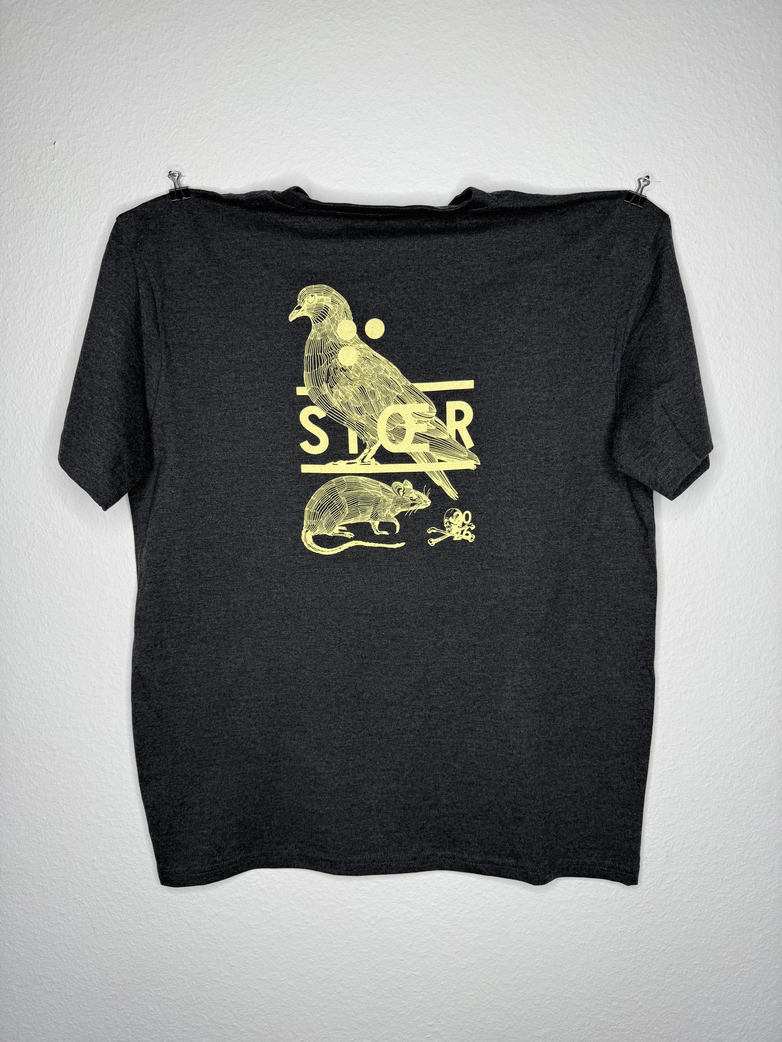 Schwarzes T-Shirt mit goldenem Vogel-, Ratten- und Totenkopf-Print, an einer weißen Wand befestigt
