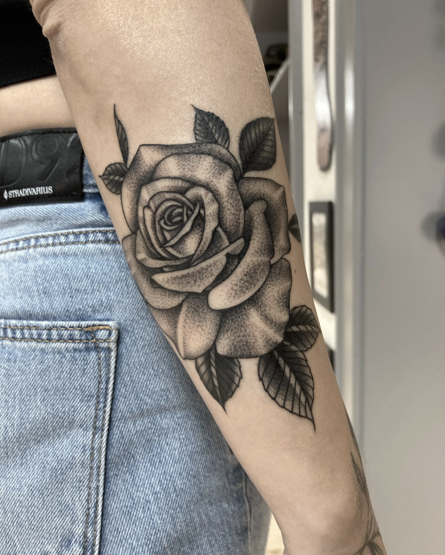 Schwarz-graues detailreiches, feines Rosentattoo mit Blättern auf einem Unterarm