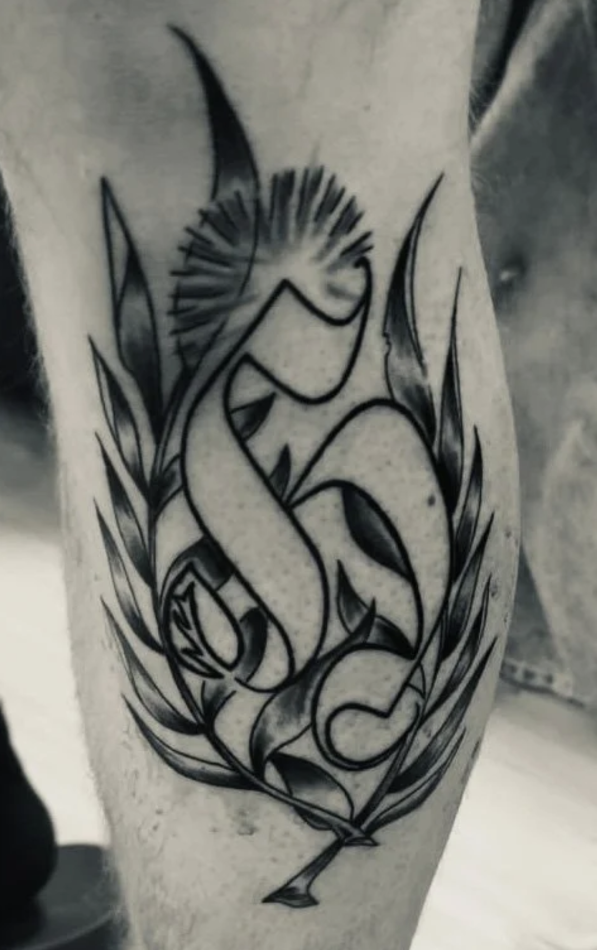 Schwarz-graues Tattoo mit stilisiertem Schwan zwischen Blättern und Gräsern am Bein