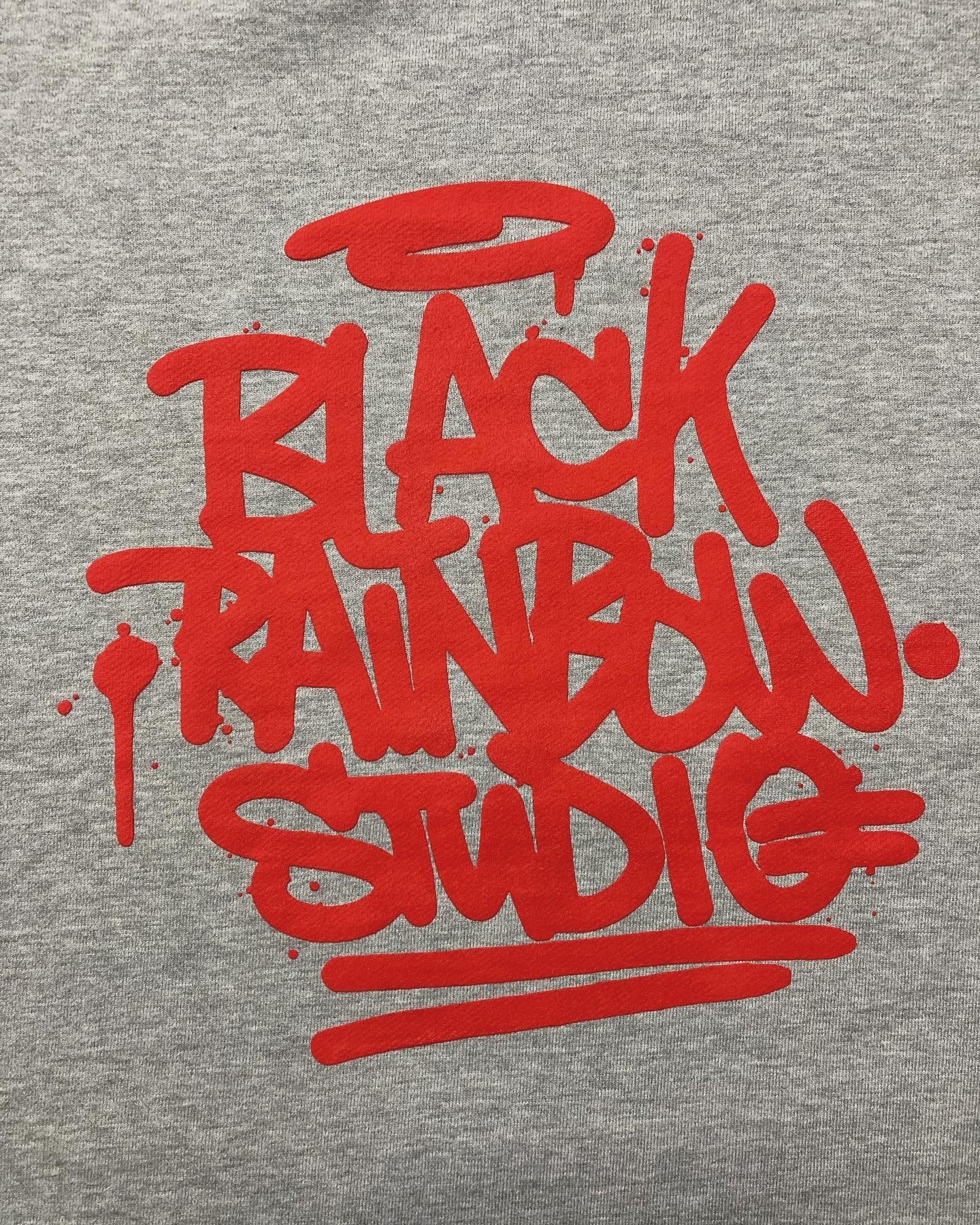 Graffitiartige rote Siebdruck Aufschrift „BLACK RAINBOW STUDIO“ auf grauem Stoff.