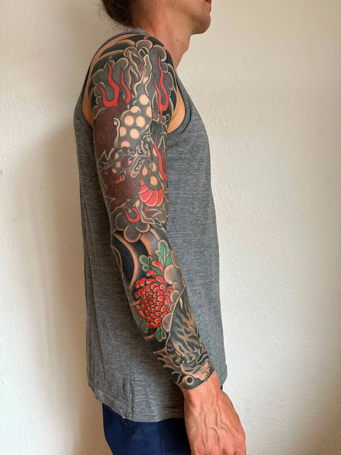 Full-Sleeve-Tattoo am Arm im traditionellen japanischen Irezumi Stil mit einer roten Chrysantheme und dunklem Wellenhintergund