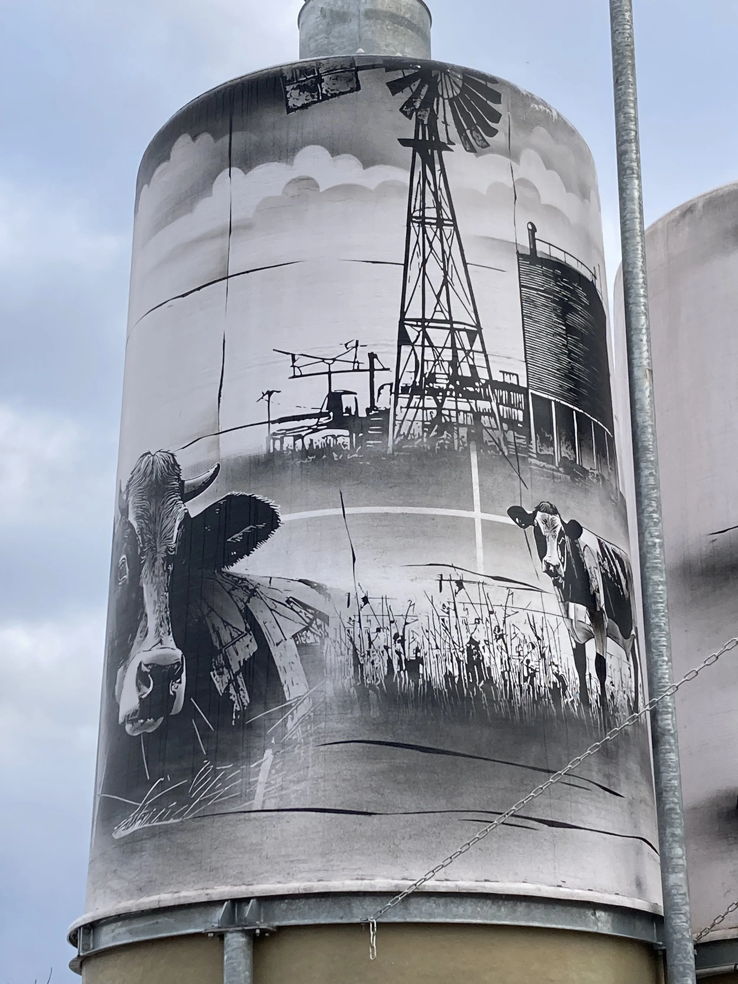 Schwarz-weiße Wandmalerei eines Kuhgesichts, eine Windmühle und eine Wasseraufbereitungsanlage auf einem großen Container