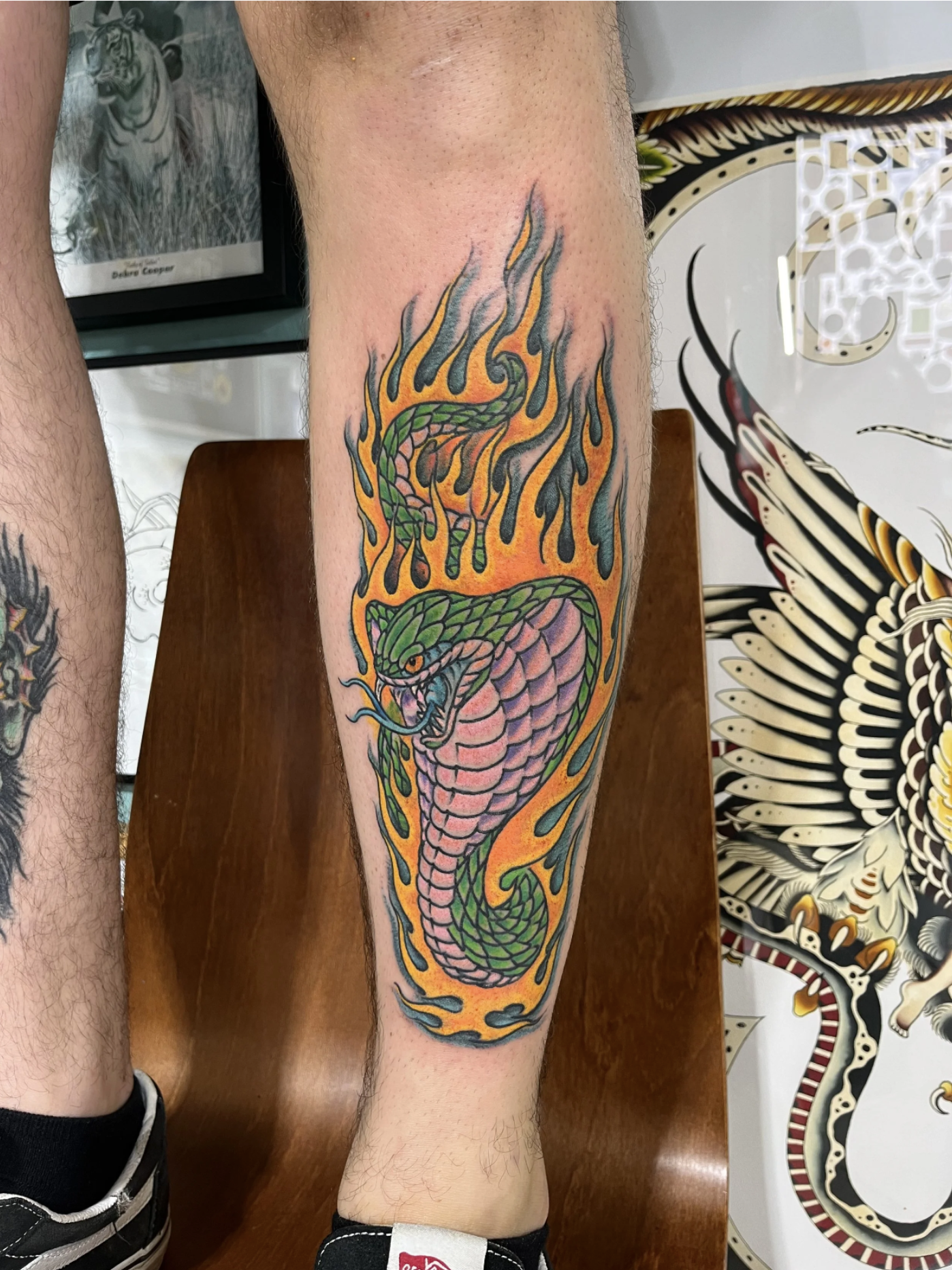 Buntes Schlangentattoo mit grüner Schlange in orangefarbenen Flammen auf dem Unterschenkel