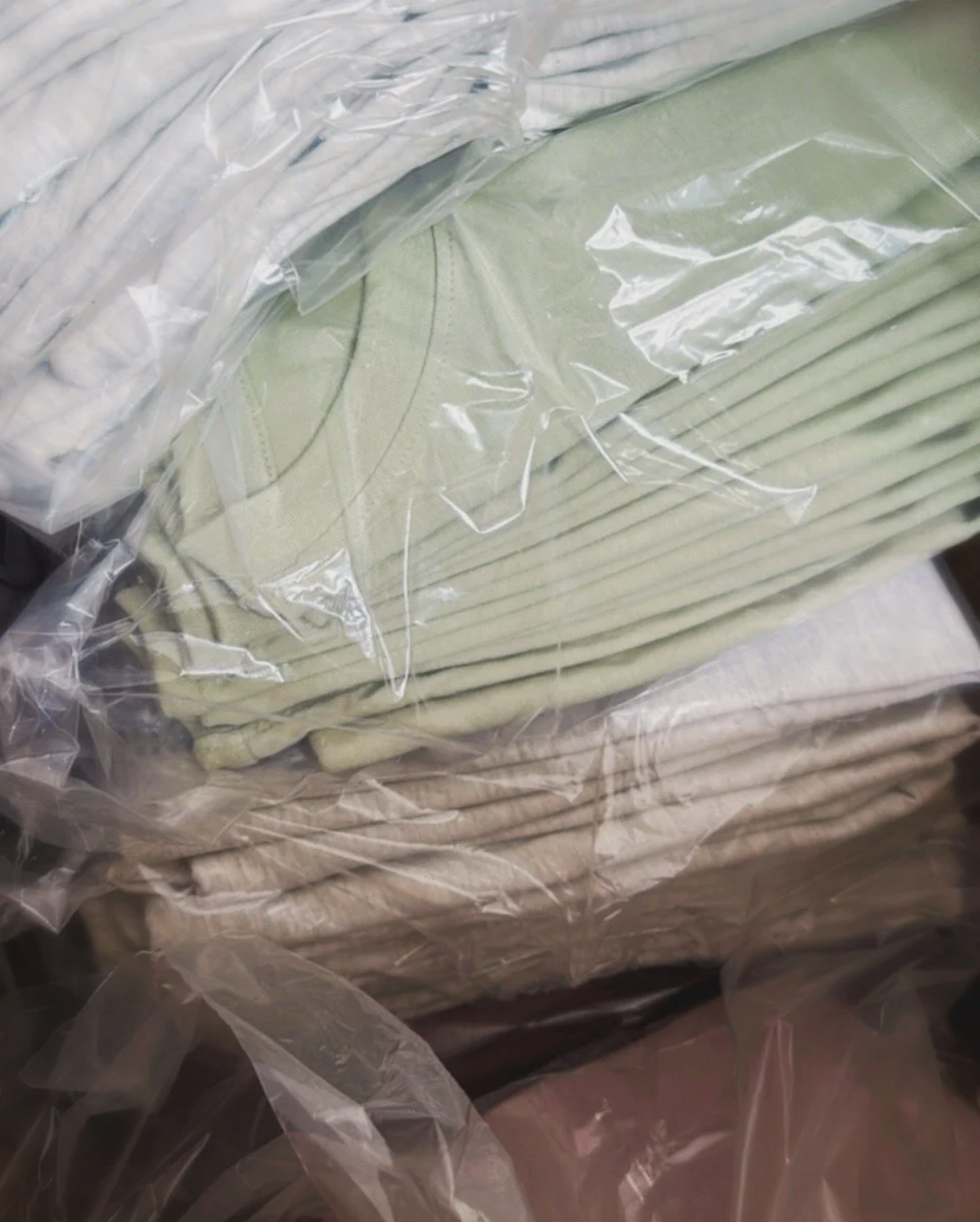 Zusammengelegte Kleidungsstücke in Pastellfarben, einzeln in durchsichtigen Plastiktüten verpackt.