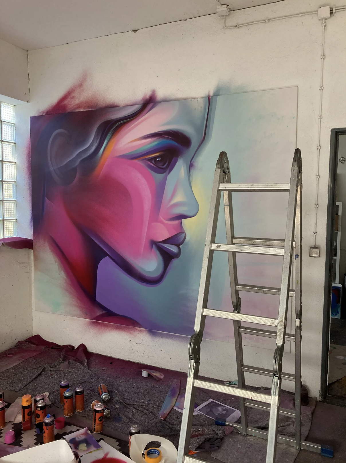 Buntes Graffiti-Porträt einer Frau in einem Atelier mit Leiter und Spraydosen