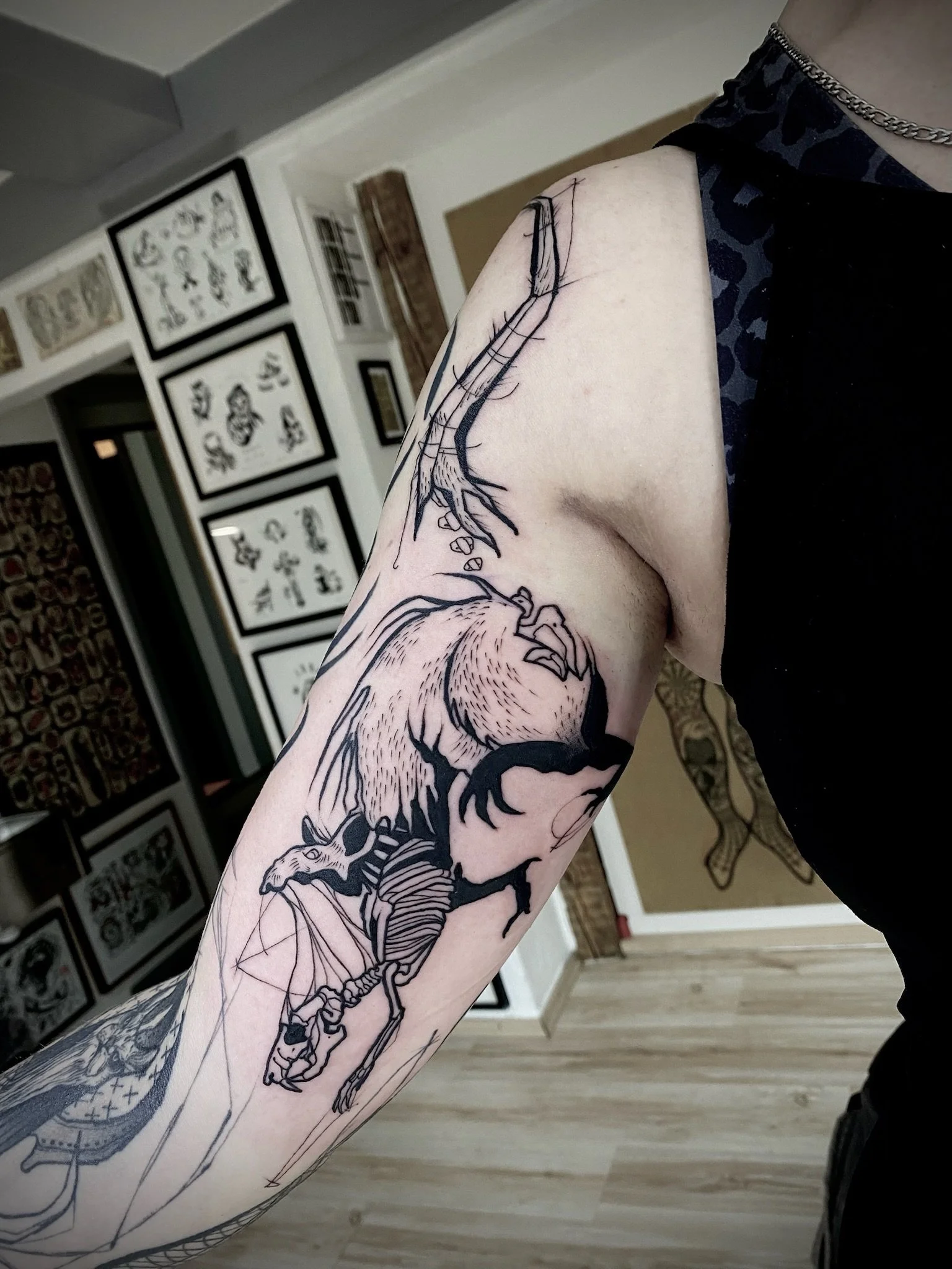 Nahaufnahme eines tätowierten Arms mit einer detaillierten Fledermaus- und Skelettillustration sowie weiteren Schwarzlinien-Tattoos