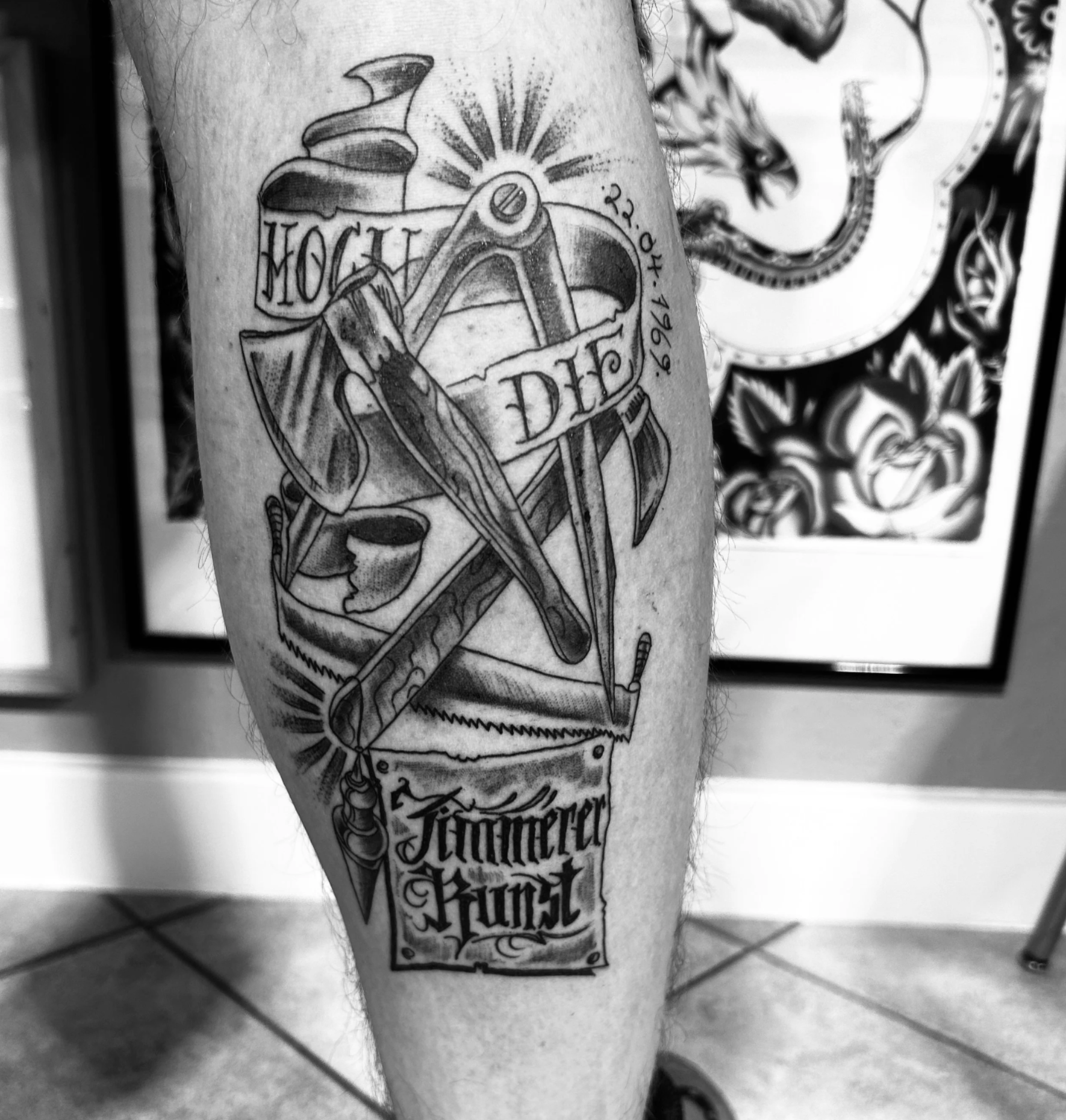 Schwarz-Weiß-Nahaufnahme eines Beintattoos mit Anker, Segelschiff, Seil, Werkzeugen und Schriftzug „Fortune Favors the Brave“.