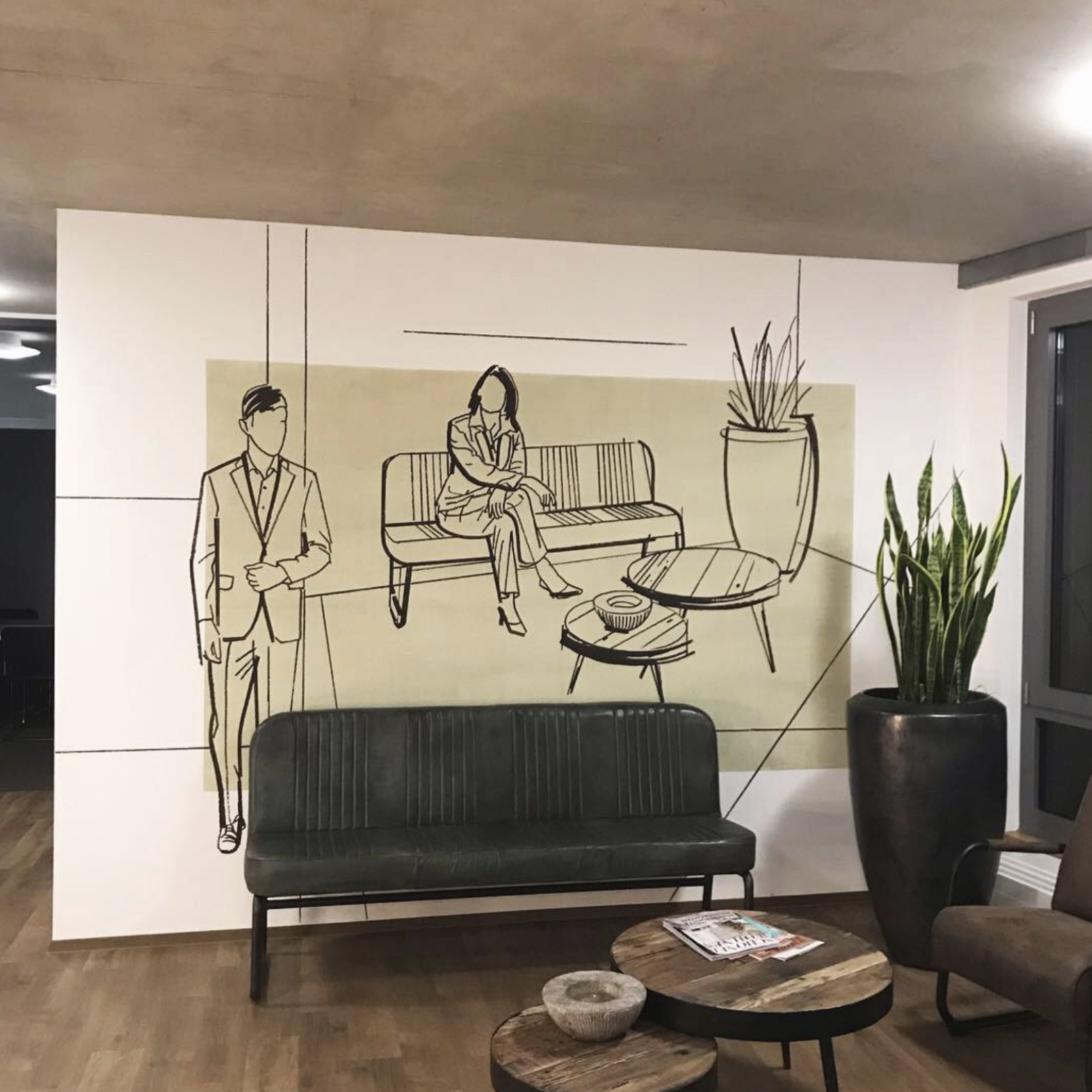 Wandillustration eines Wartezimmers mit zwei Menschen, einem Mann und einer Frau, und einigen Pflanzen. Die Illustration ist schwarz-weiß, während die Umgebung in natura gestaltet ist.