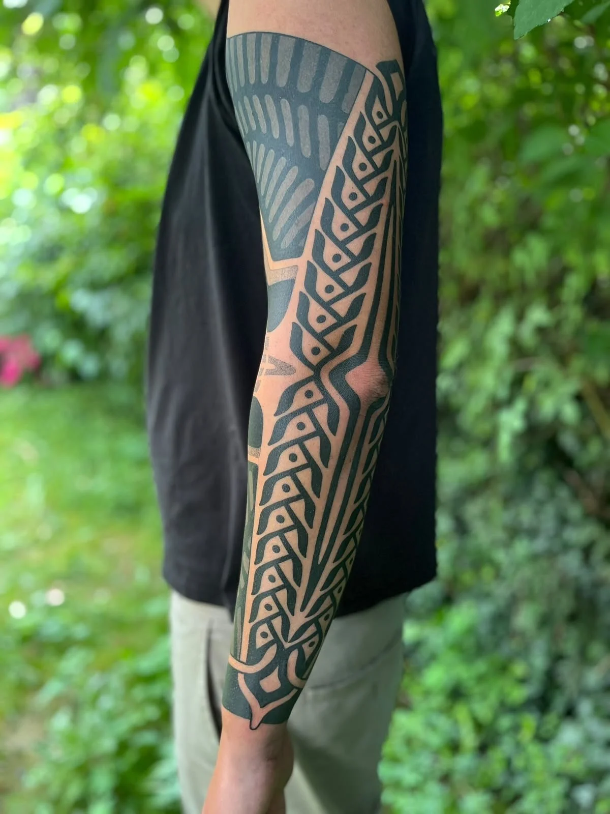 Nahaufnahme eines Arms mit großflächigem schwarzem geometrischem Blackwork Tattoo vor grünem Pflanzenhintergrund