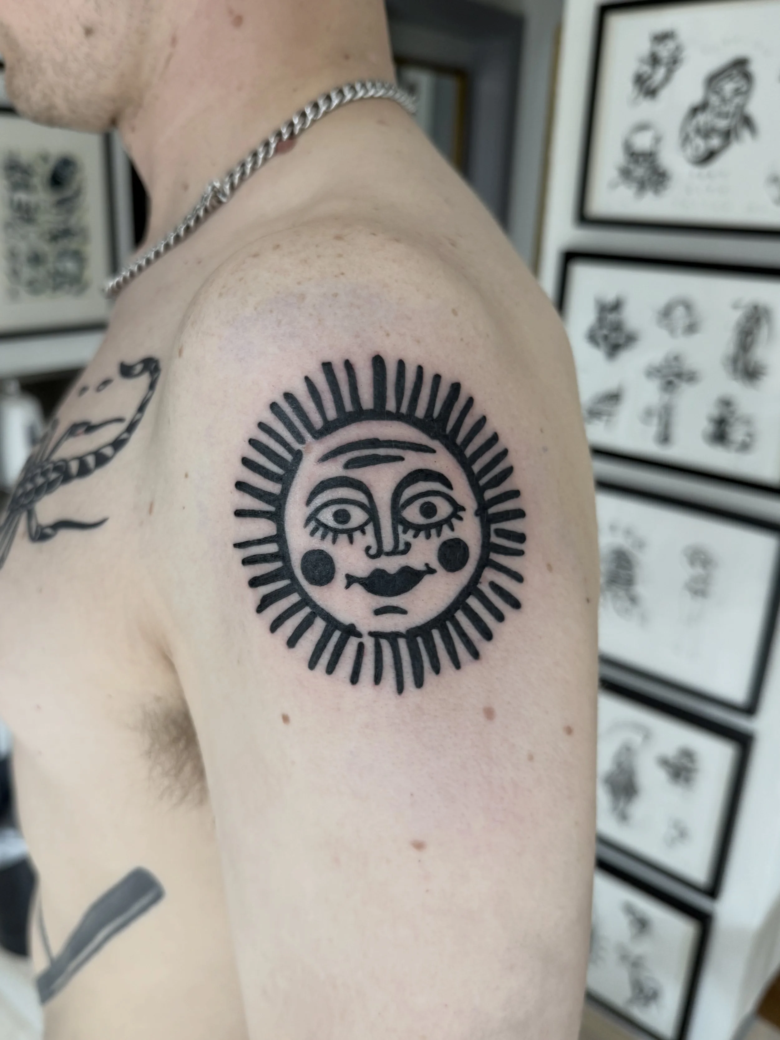 Nahaufnahme eines Oberarms mit schwarzem Tattoo einer stilisierten Sonne