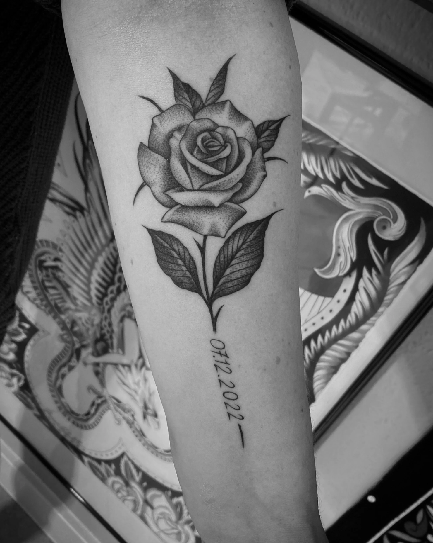 Schwarz-weißes Rosentattoo mit Blättern und dem Datum 07.12.2022 auf einem Unterarm