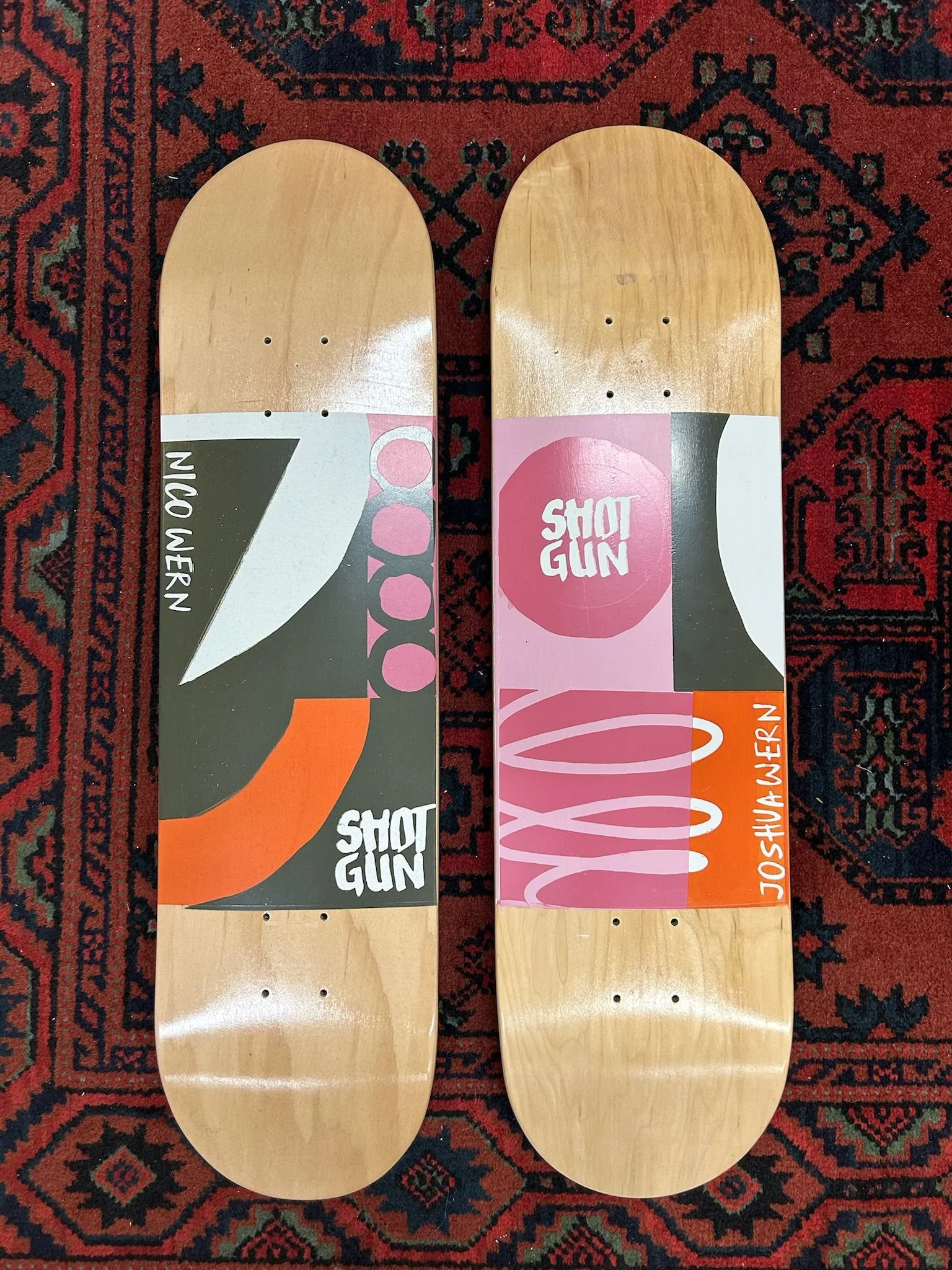 Zwei rohe Skateboarddecks mit farbenfrohen Grafiken liegen nebeneinander auf einem roten Orientteppich.