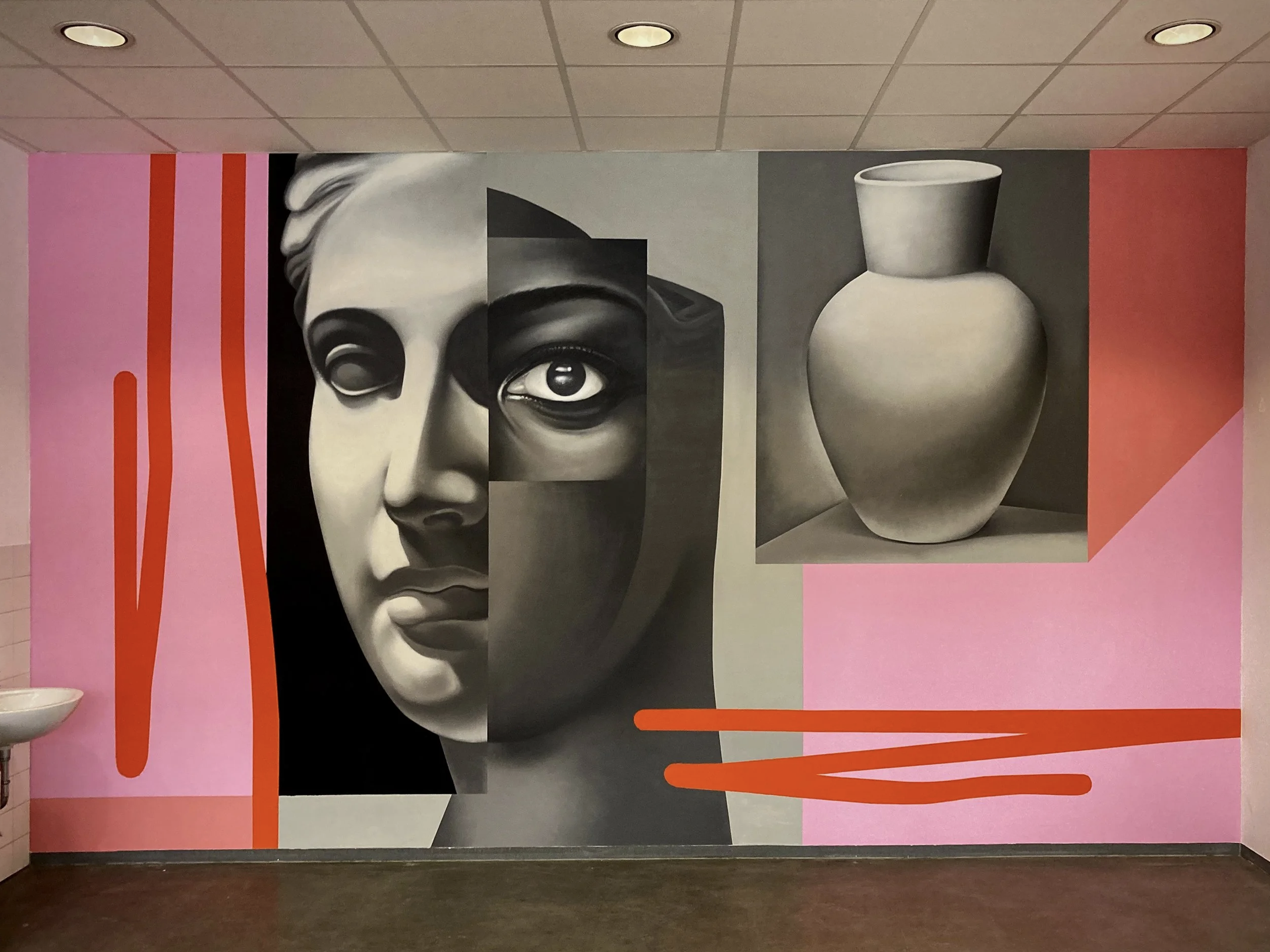 Moderne Wandkunst mit einem stilisierten schwarzen und weißen Gesicht einer Frau, die teilweise aus geometrischen Formen besteht, neben einer weißen Vase, auf einer pinkfarbenen Wand mit roten Akzenten.