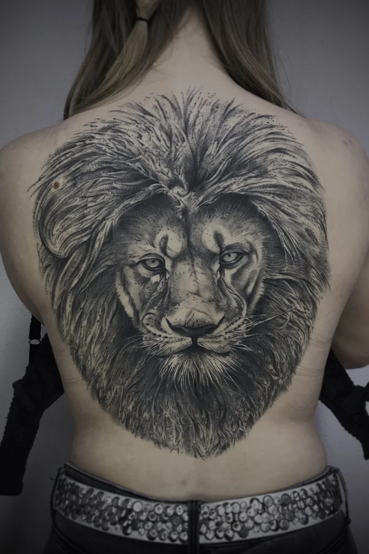 Großflächiges Schwarz-Grau-Tattoo eines realistischen Löwenkopfs auf dem oberen Rücken einer Person