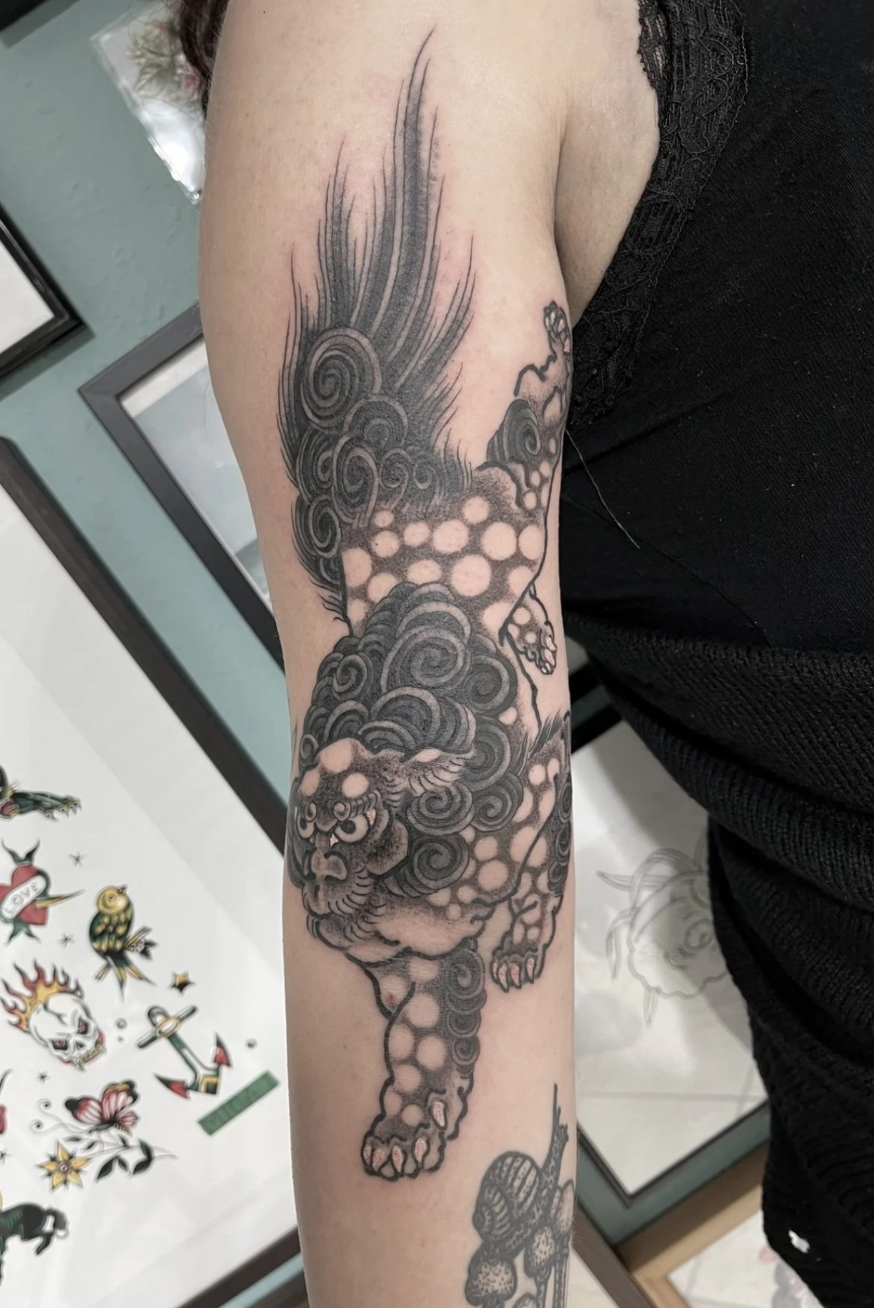 Schwarz-graues Tattoo eines stilisierten Löwen mit Wolken- und Spiralmotiven auf dem Oberarm