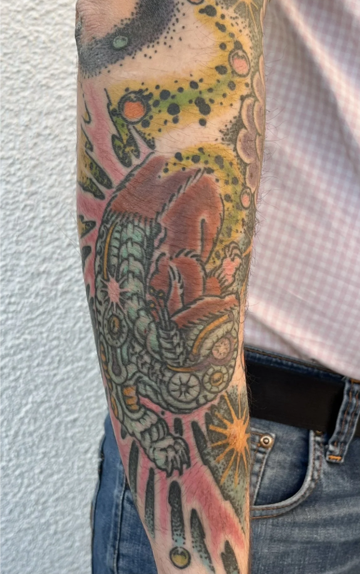 Nahaufnahme eines bunten, floralen Tattoo-Ärmels mit Blumen, Blättern und abstrakten Mustern auf einem Arm.