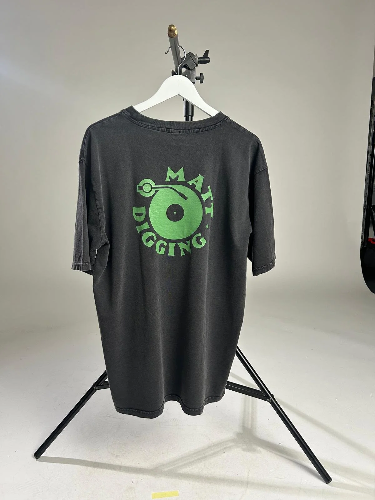 Anthrazitfarbenes T-Shirt auf weißem Kleiderbügel mit grünem DJ-Logo und Schriftzug