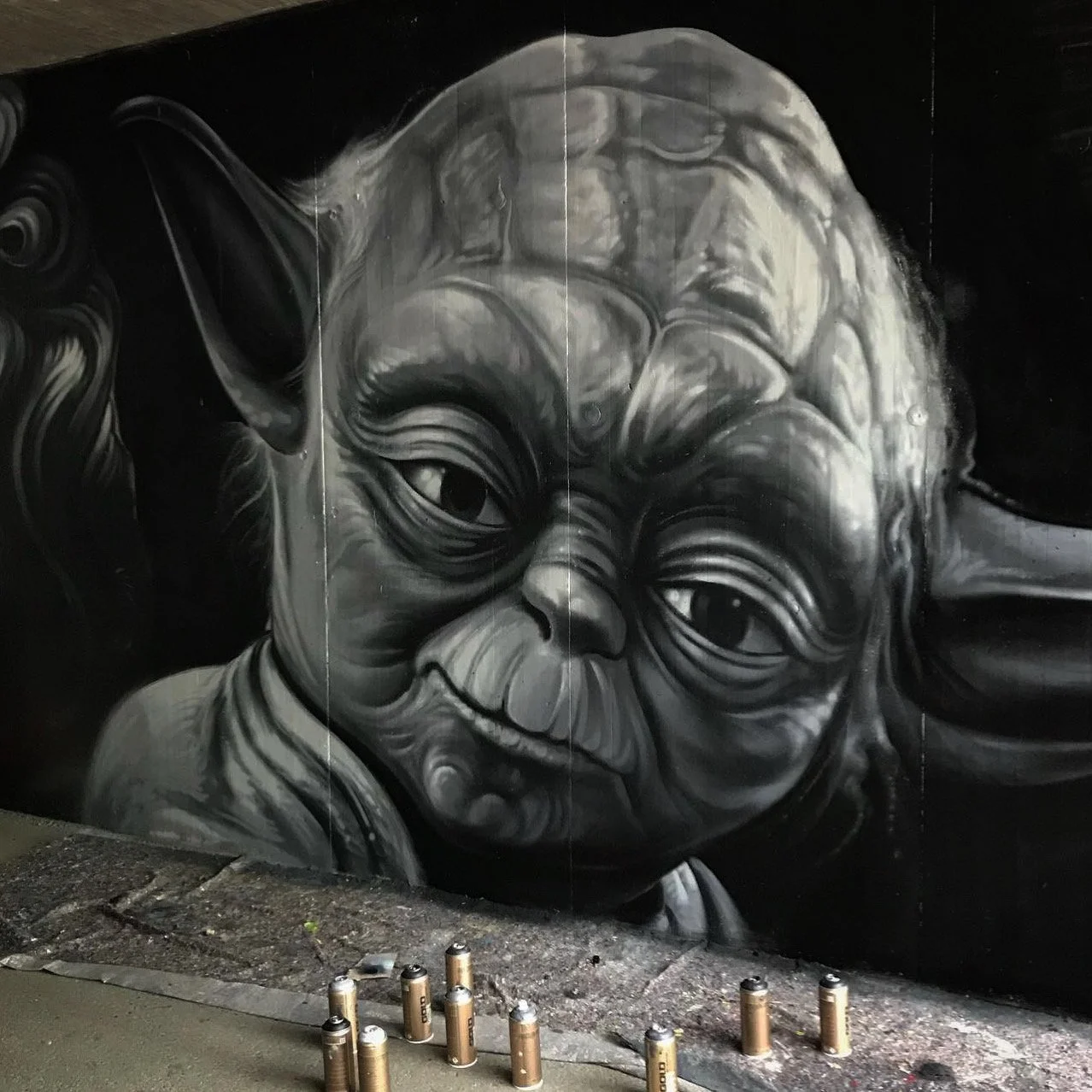 Graffiti-Kunstwerk das Yoda von Star Wars zeigt. Spraydosen liegen vor der Wand.