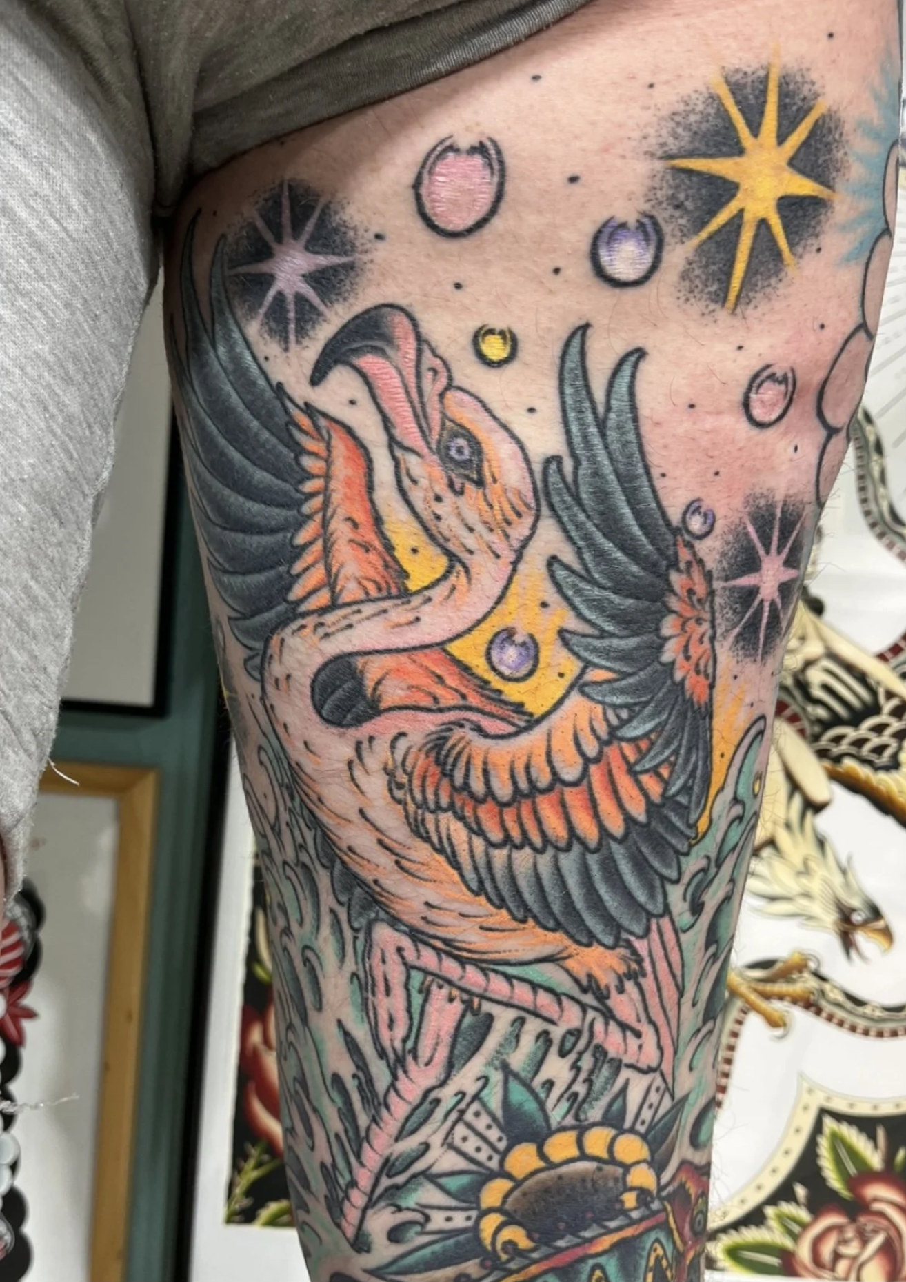 Nahaufnahme eines farbenfrohen Tattoo-Ärmels mit stilisiertem Flamingo, Sternen, Blumen und dekorativen Mustern.