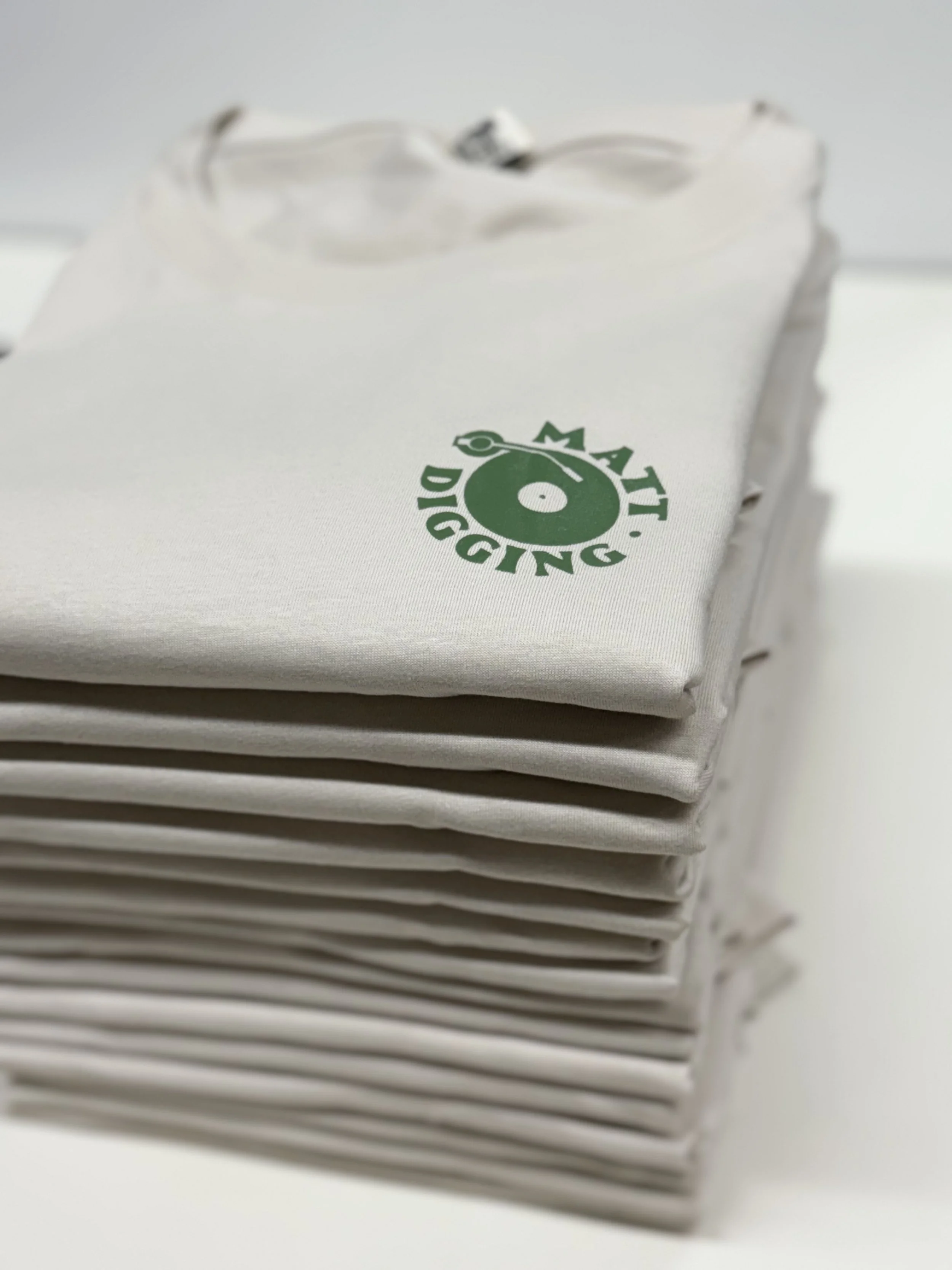 Stapel weißer T-Shirts mit grünem, kreisförmigem Logo und Schriftzug
