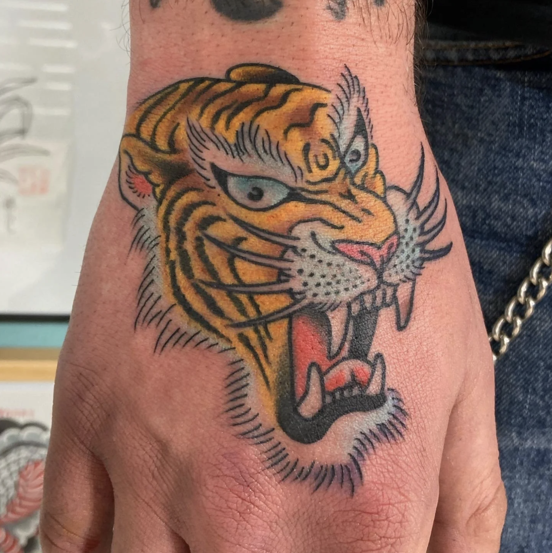 Nahaufnahme eines farbigen Tigerkopfs als Tattoo auf einer Hand
