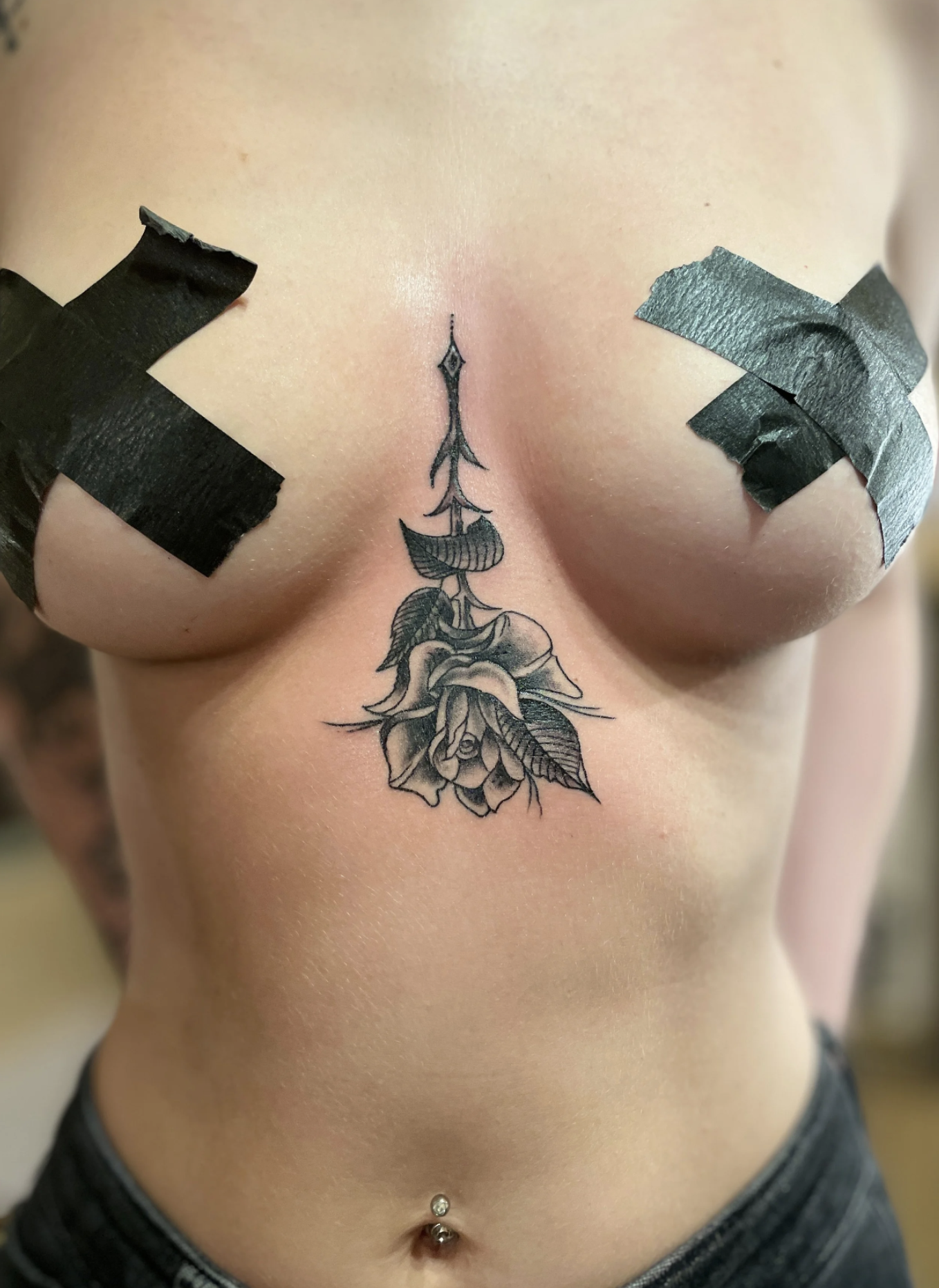 Frisches florales Tattoo zwischen den Brüsten mit schwarzem Wundklebeband und Bauchnabelpiercing