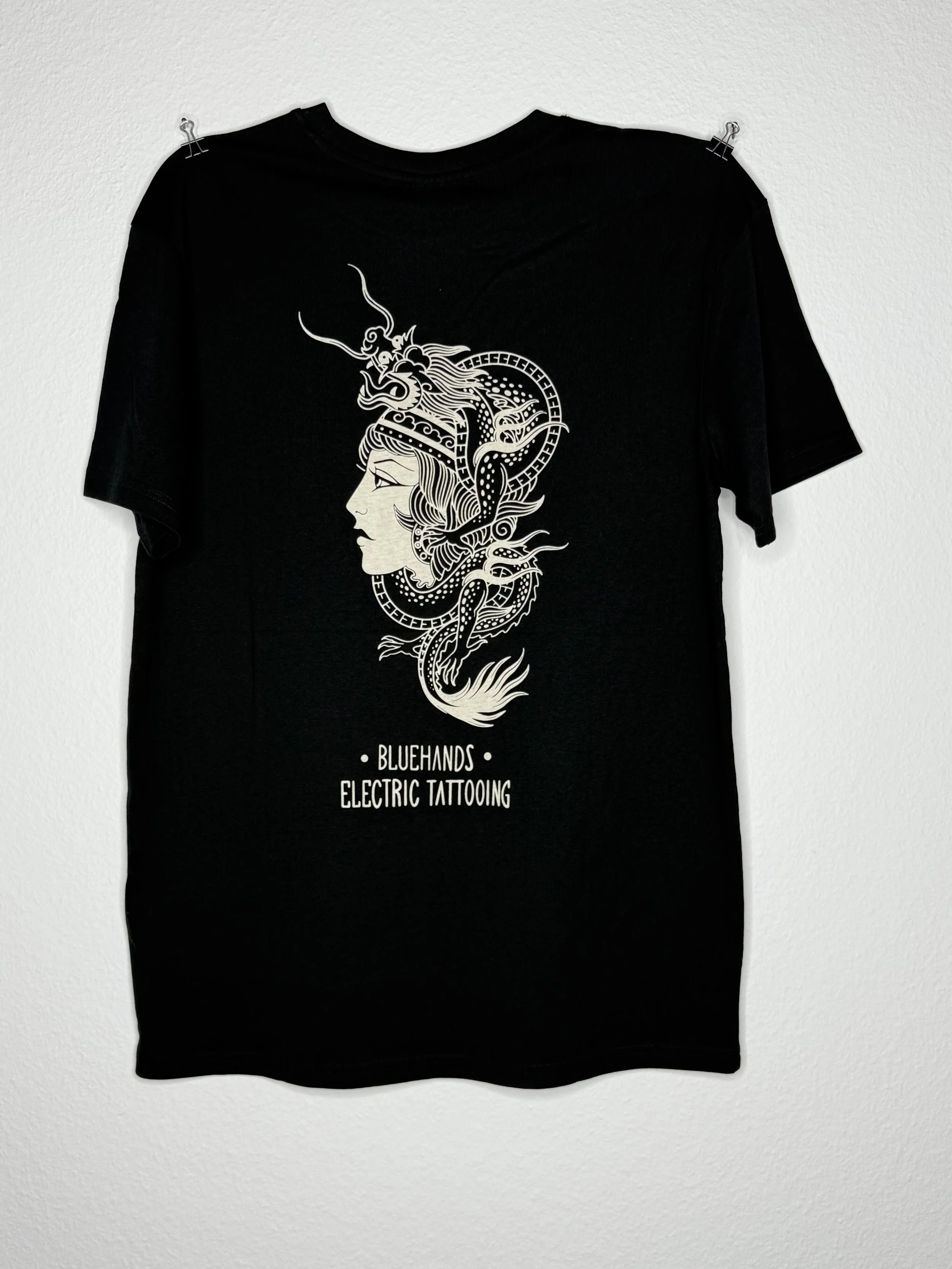 Schwarzes T-Shirt mit weißem Drachen- und Frauenprofil-Motiv sowie dem Schriftzug „BLUEHANDS ELECTRIC TATTOOING“