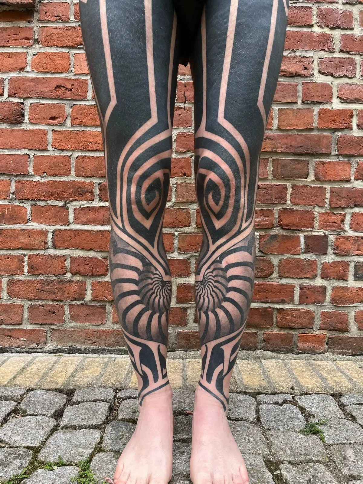 Beine mit auffälligen schwarzen geometrischen Tattoos vor einer roten Backsteinwand