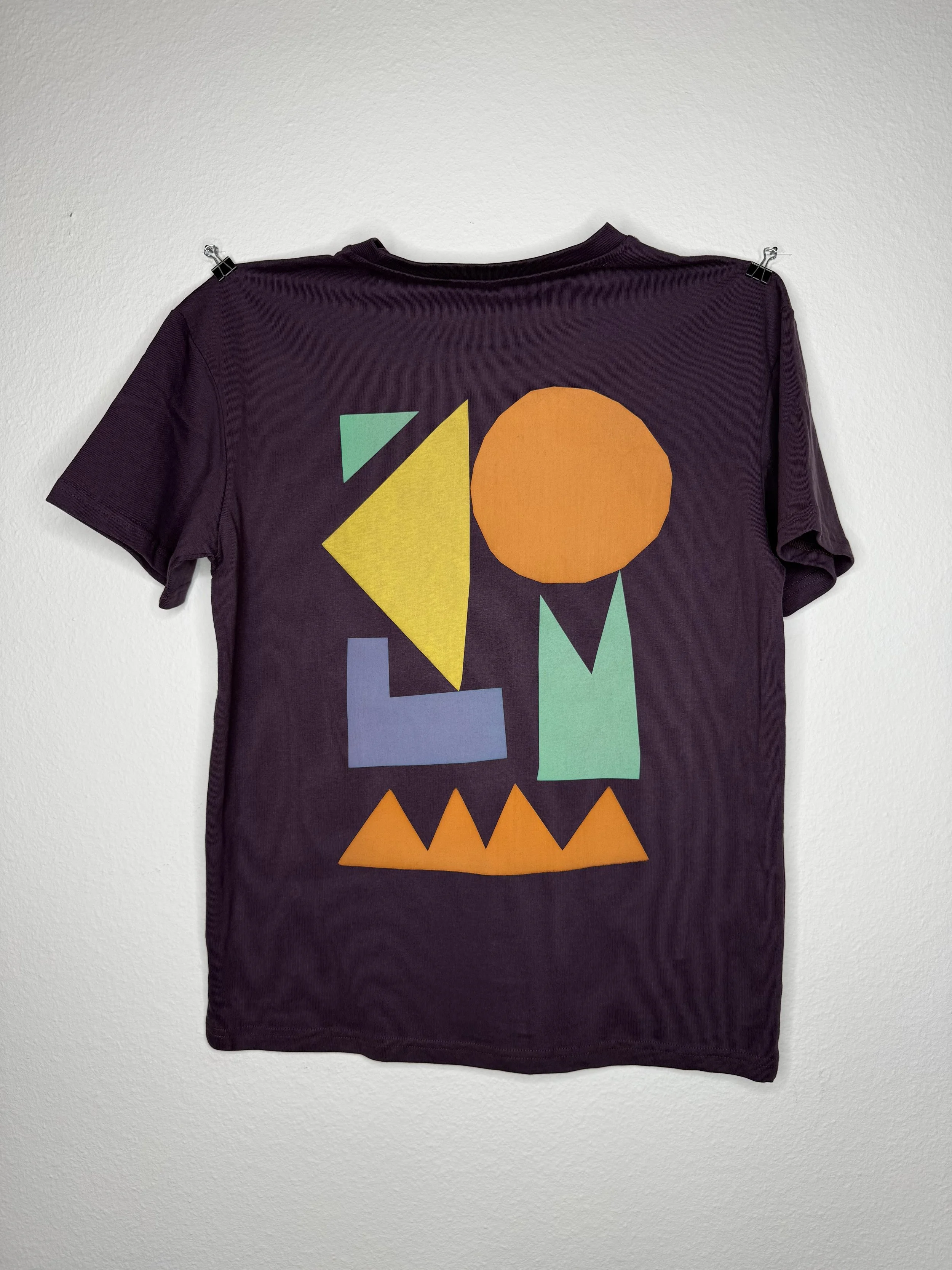 Dunkelviolettes T-Shirt mit farbenfrohem geometrischem Muster, an einer weißen Wand befestigt